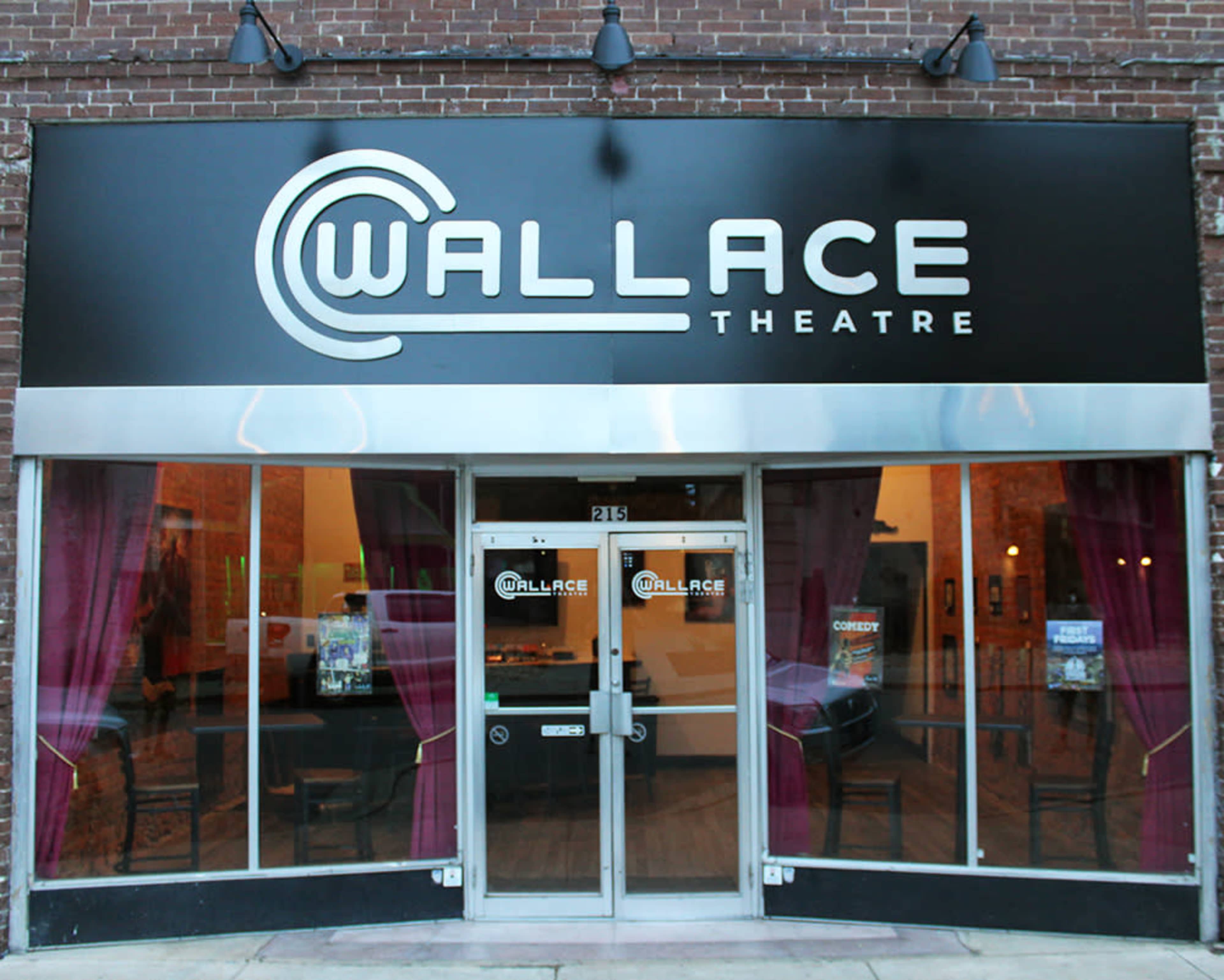 The image shows the front exterior of the Wallace Theatre, featuring large signage and glass doors with a simple decorative facade.