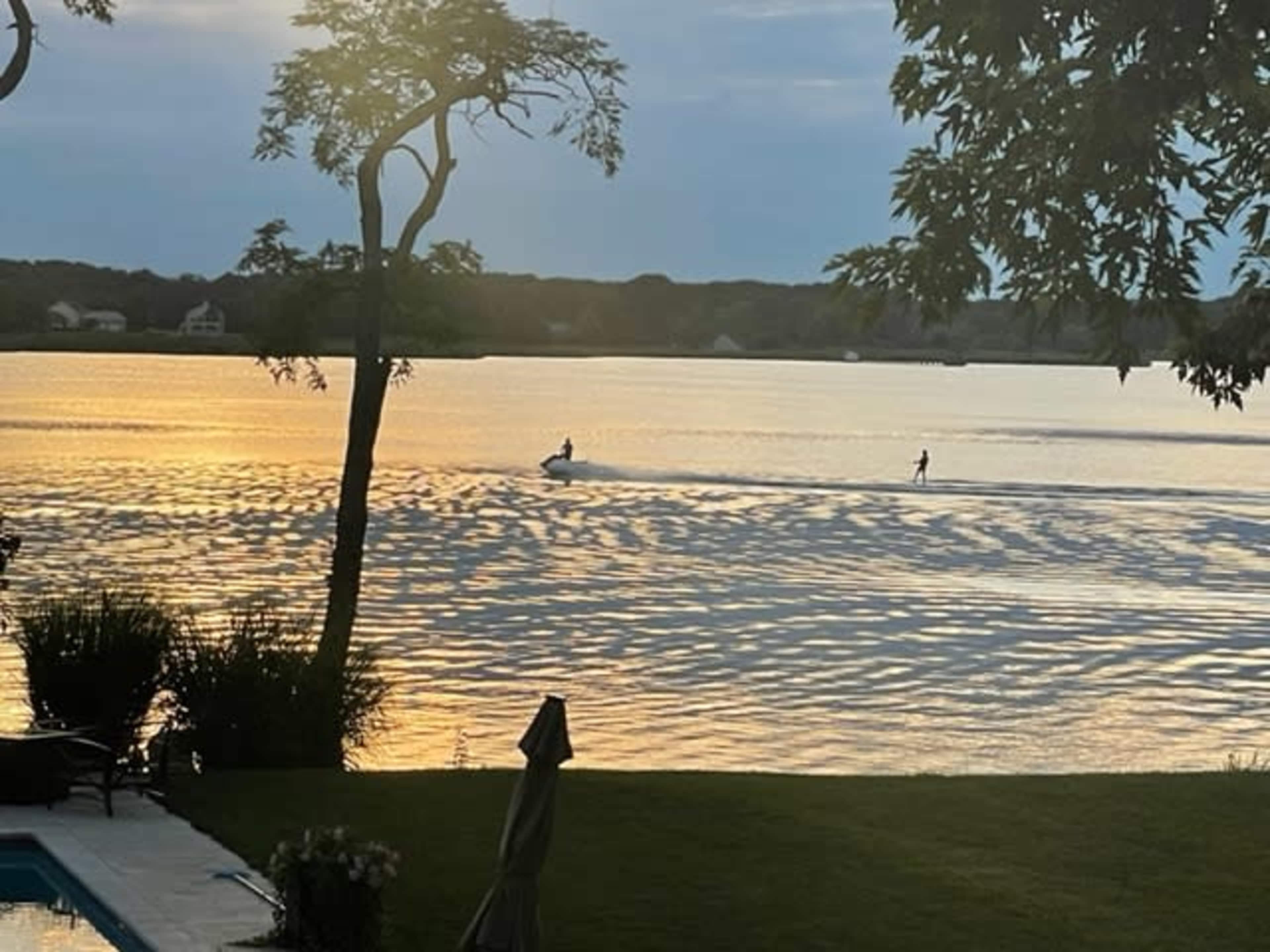 A person water skis behind a boat on a rippling lake at sunset.