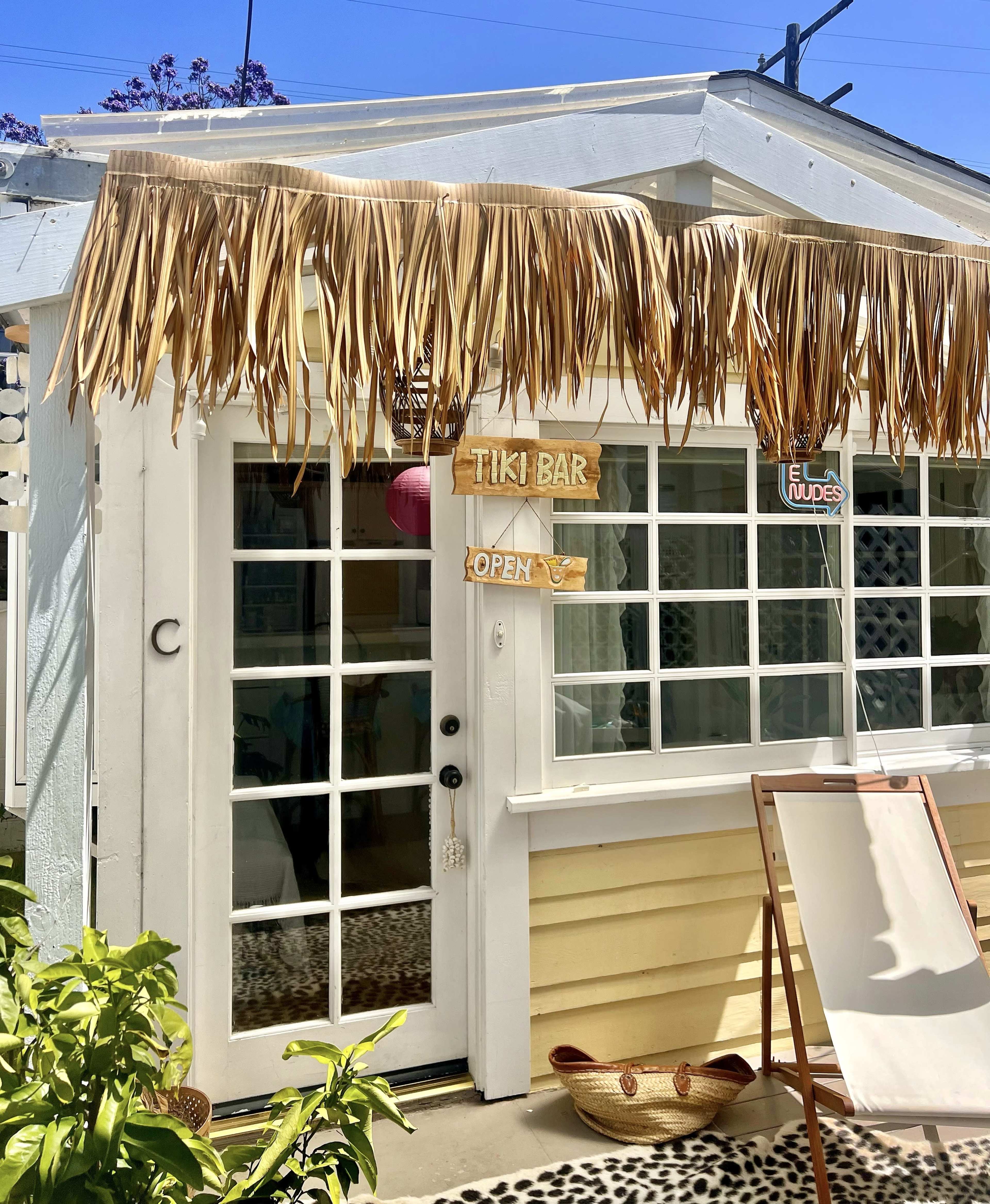 A small tiki bar with a thatched roof, an "Open" sign, and a lounge chair outside.