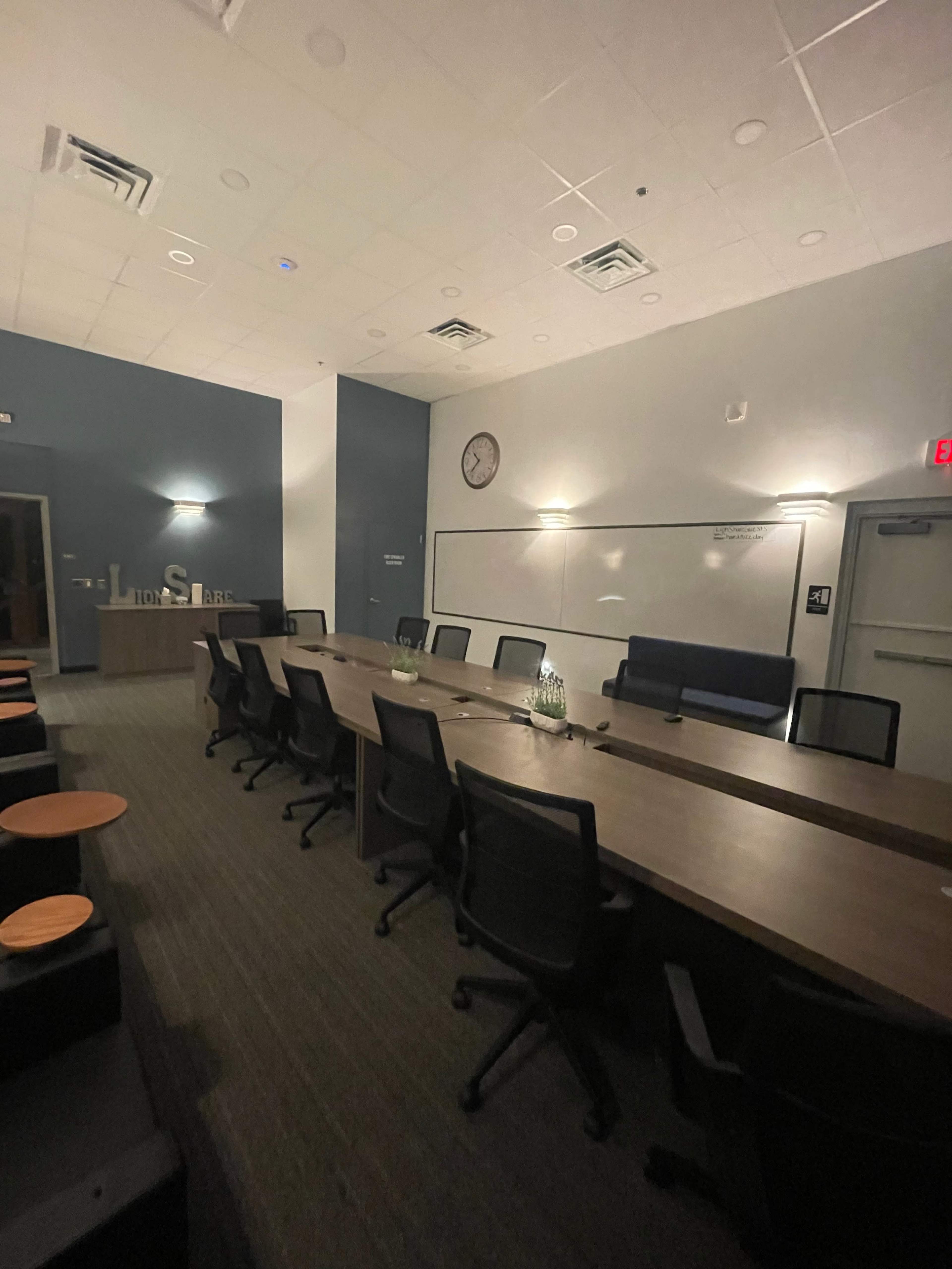 A large conference room with a long table, chairs, a clock on the wall, and a whiteboard.