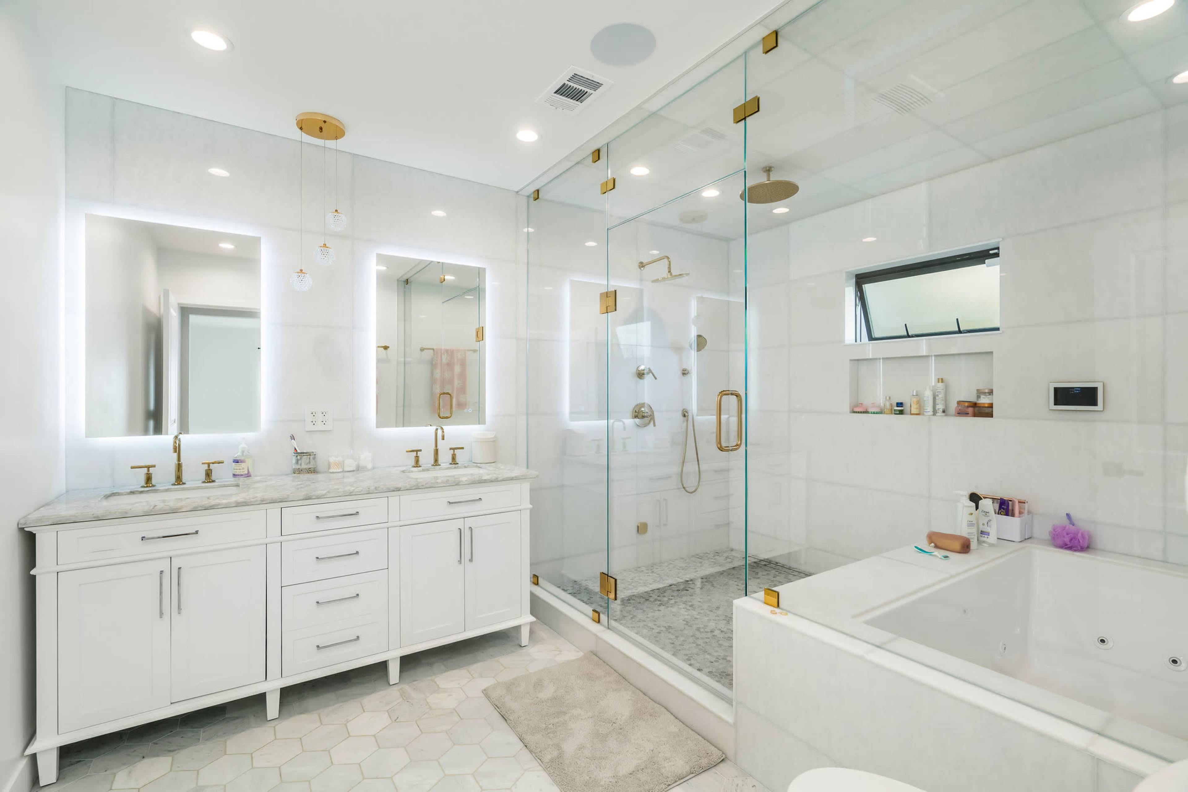 The image shows a modern bathroom featuring a glass shower enclosure, a large vanity with double sinks, and a freestanding bathtub.