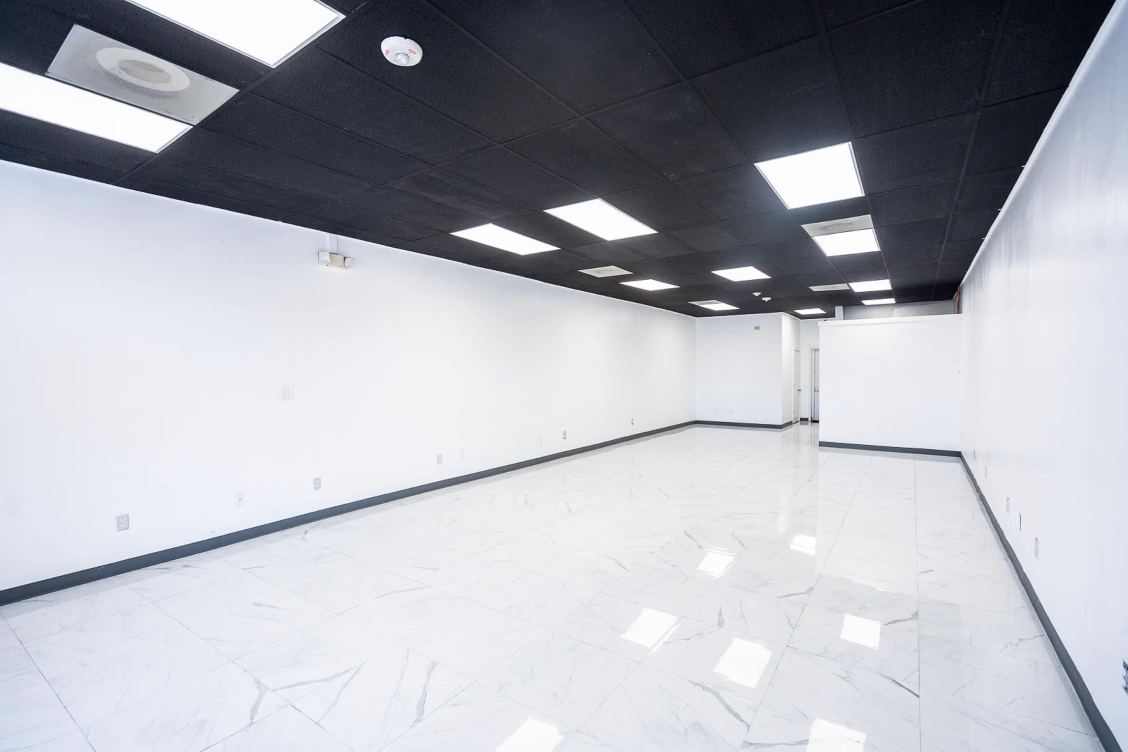 The image shows a vacant room with white walls and a glossy tiled floor, illuminated by fluorescent ceiling lights.
