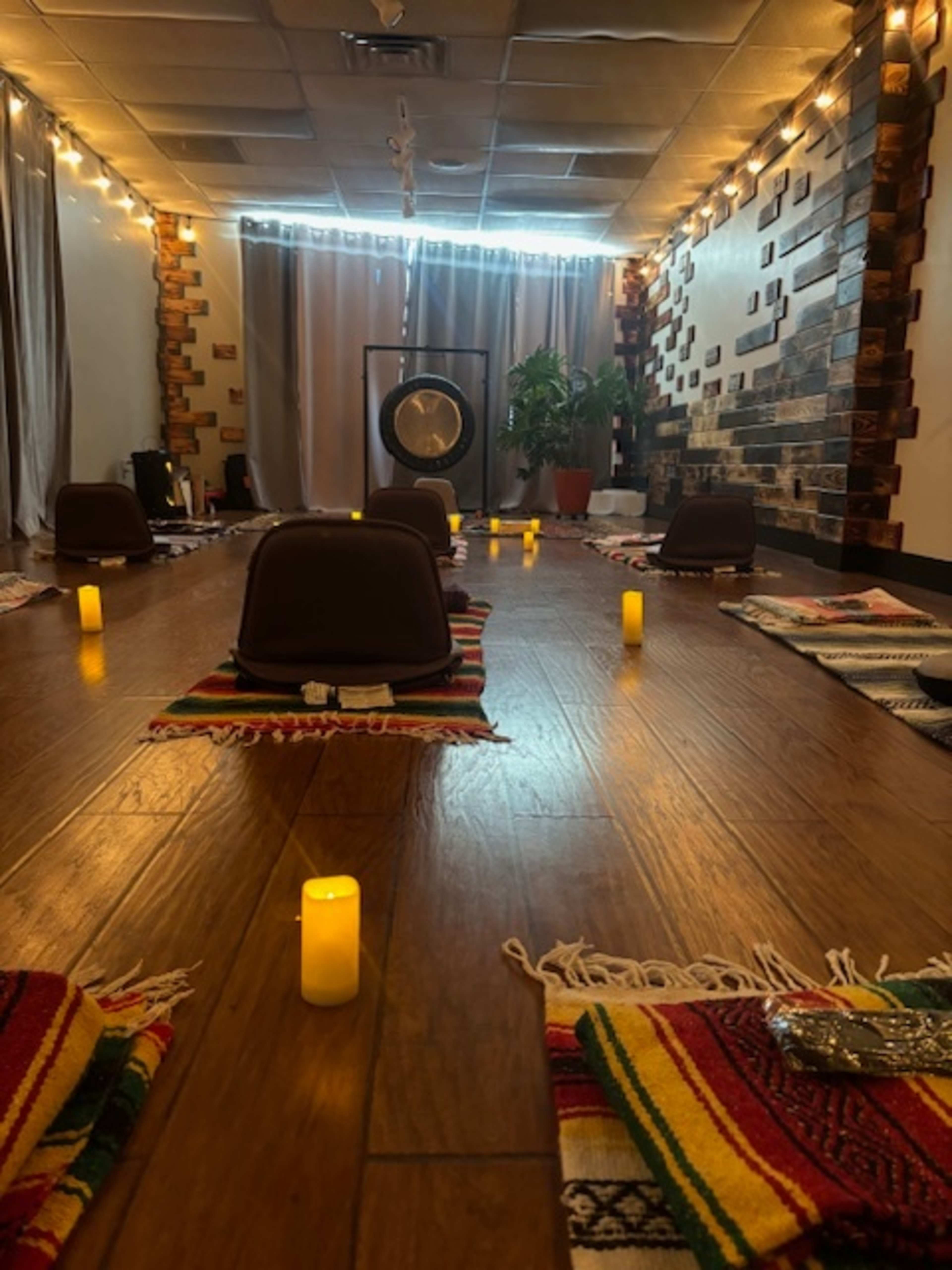 The image shows a meditation space with mats and low stools arranged in rows, illuminated by candles and featuring a gong at the front.