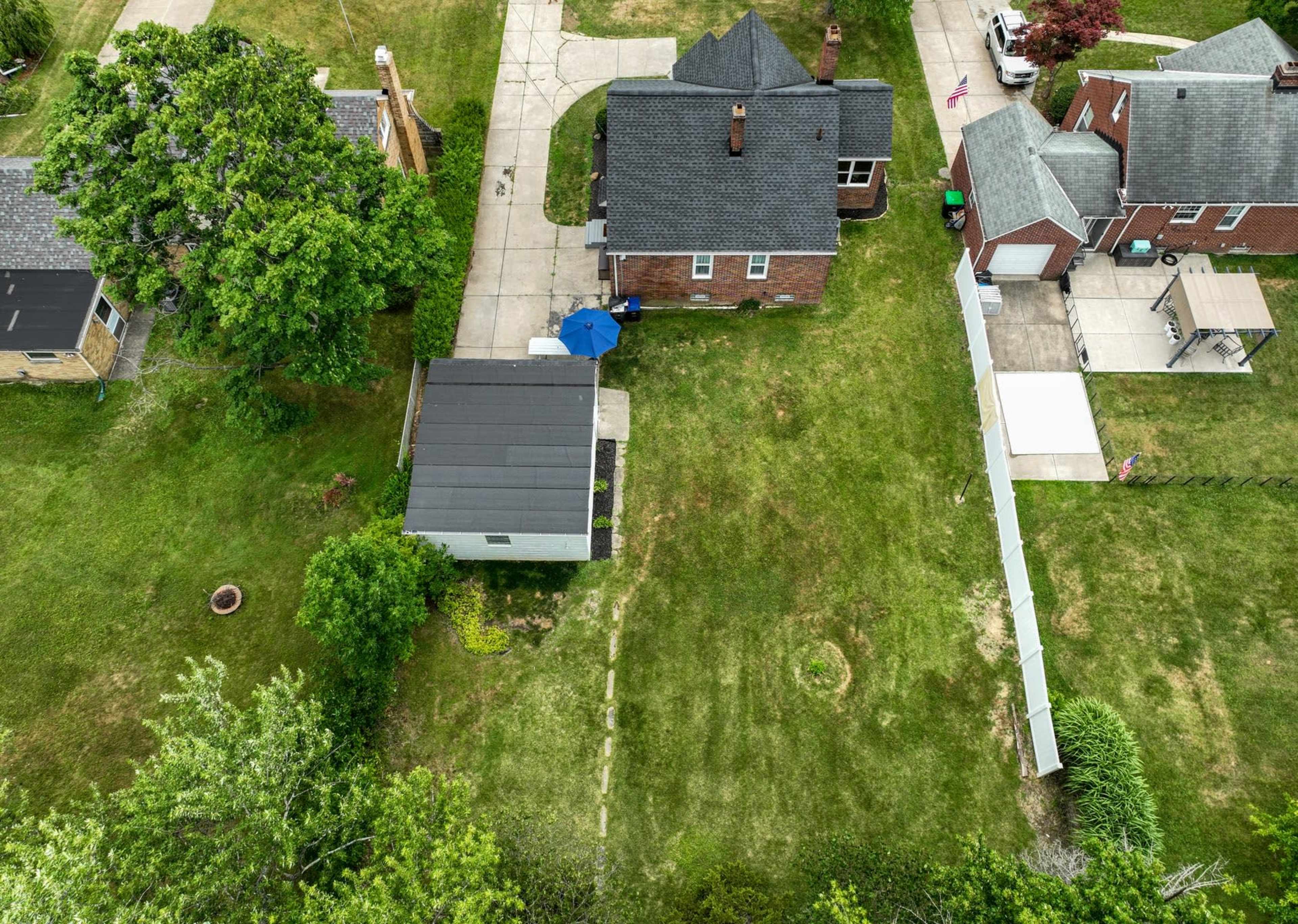 An aerial view of several residential properties with varying roof styles and a backyard featuring a shed and a blue umbrella.