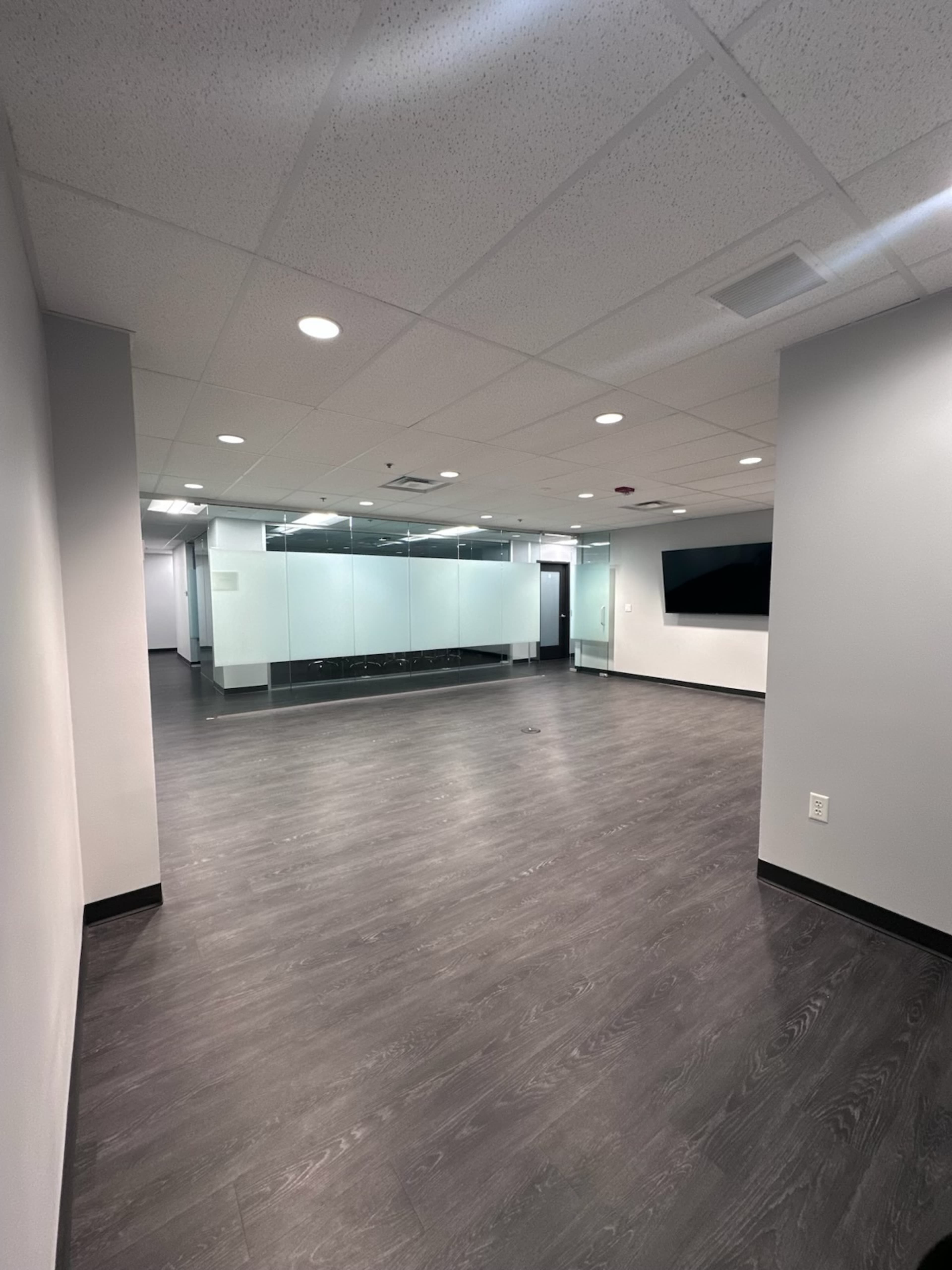The image shows a modern office space with a large open area and glass-walled meeting rooms.