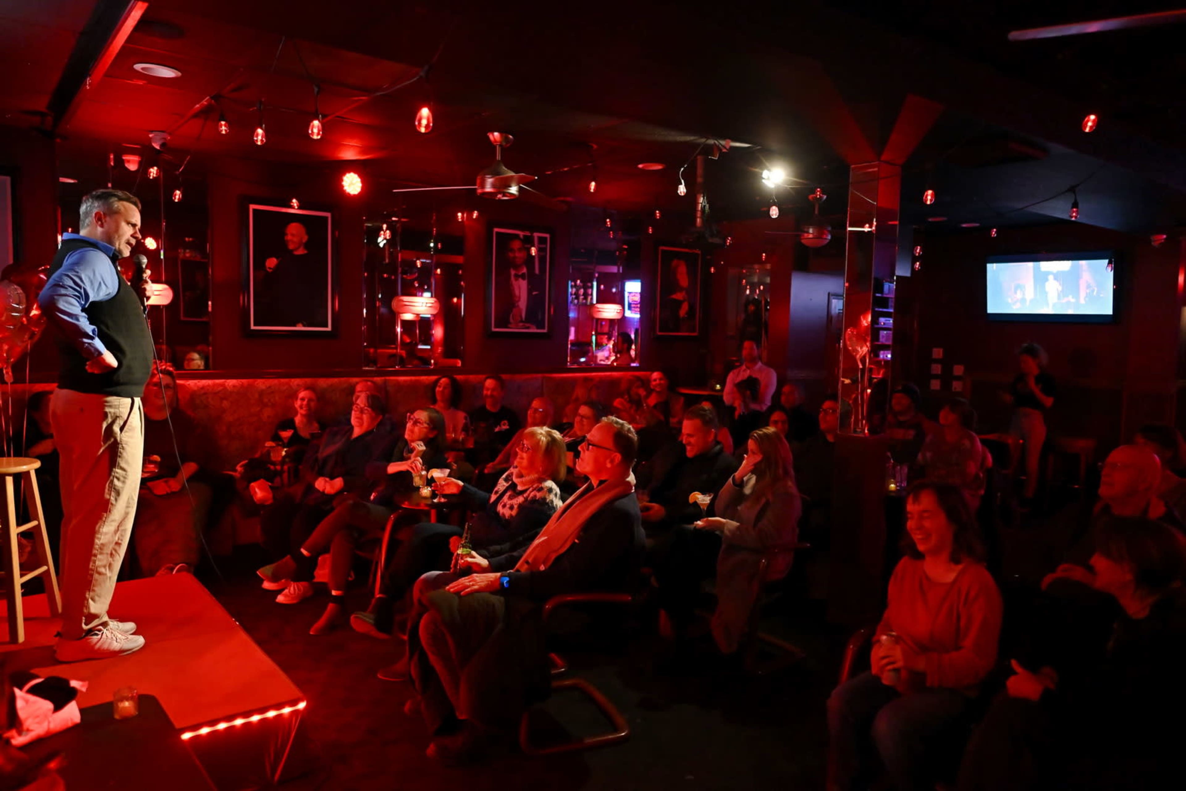 A comedian performs on stage in a dimly lit comedy club while an audience watches attentively.