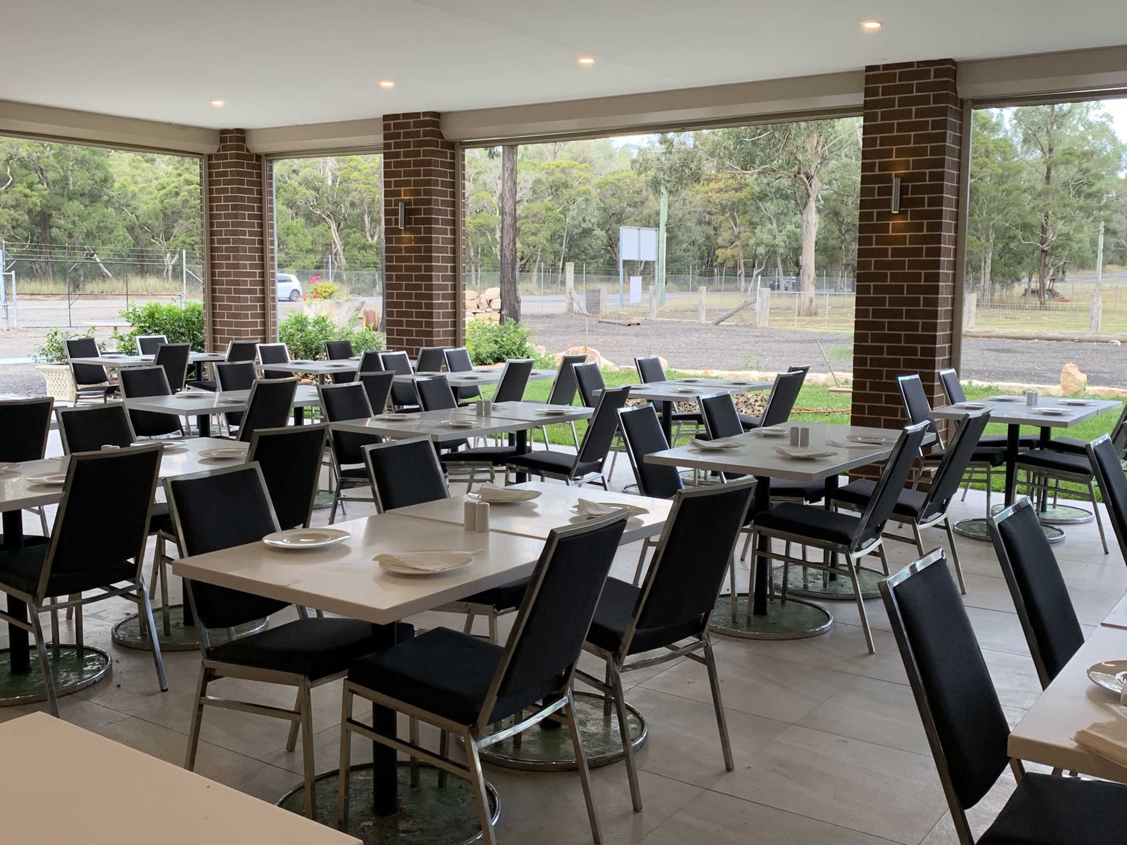 A spacious dining area with gray tables and chairs arranged neatly, surrounded by large windows overlooking a green landscape.
