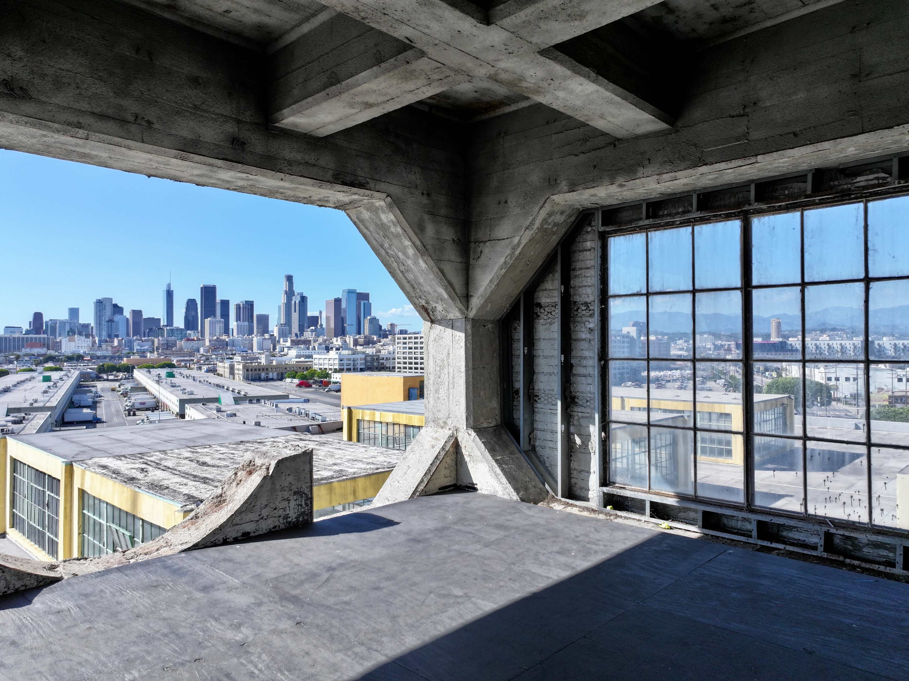 A view of the Los Angeles skyline from an industrial-style interior with large windows and exposed concrete beams.