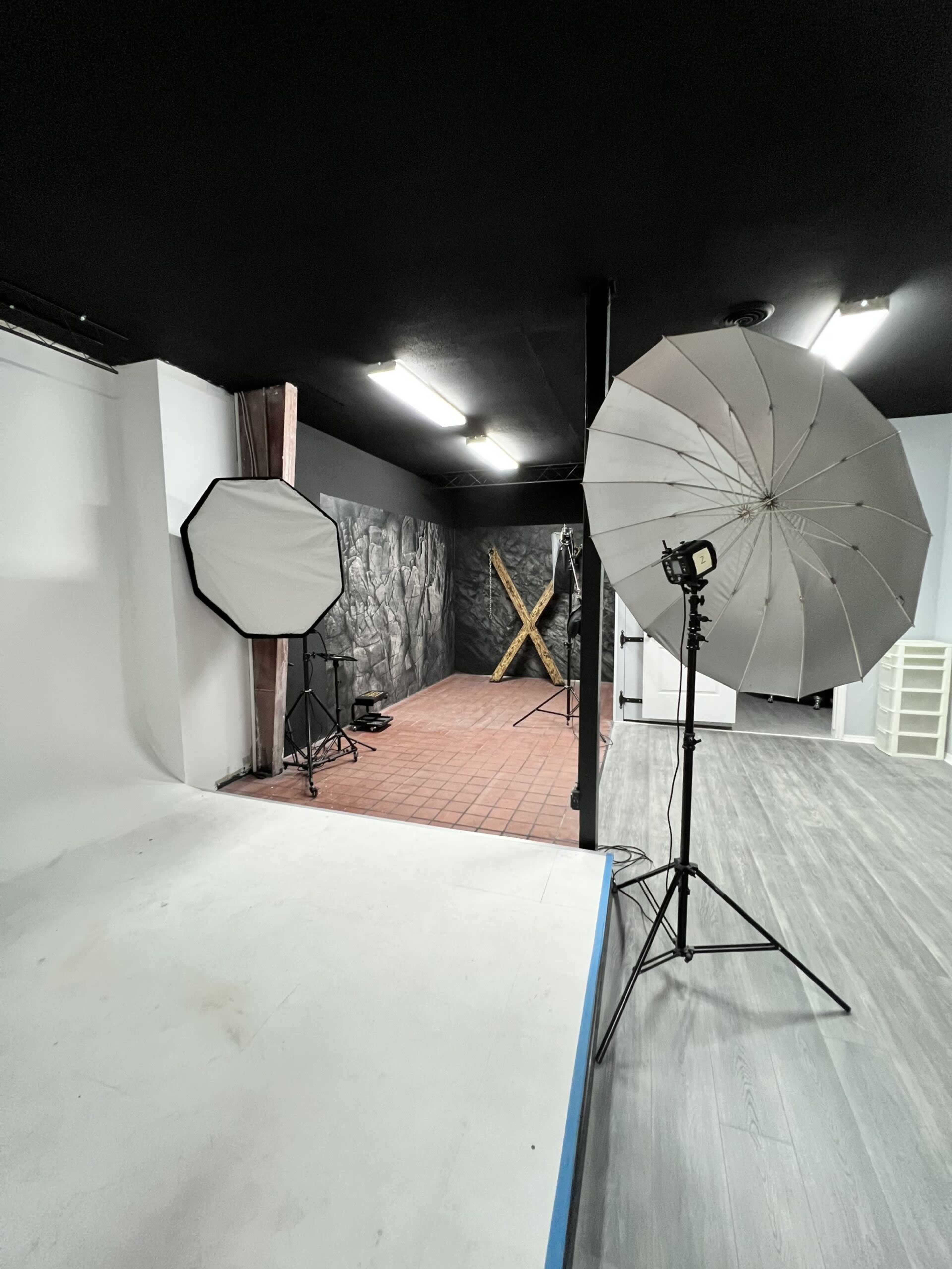 A photography studio features an empty backdrop with lighting equipment set up on either side.