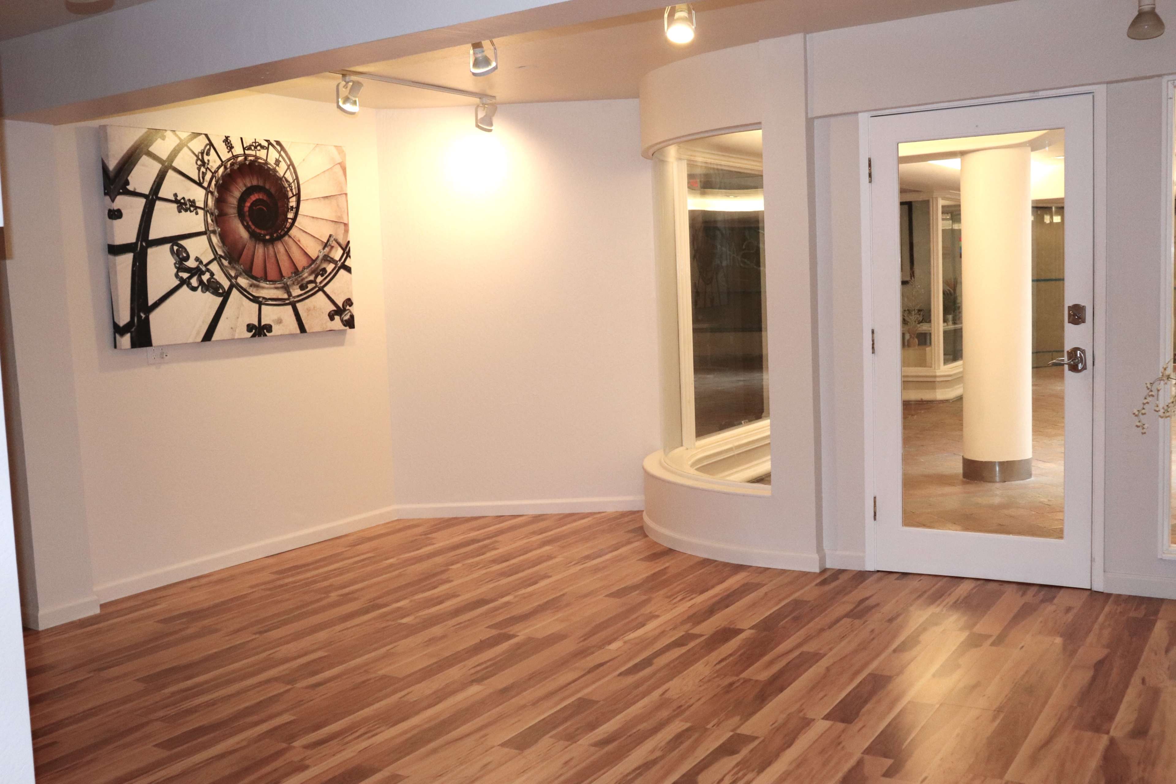A modern interior space with a wooden floor, a large spiral staircase artwork on the wall, and a rounded window beside glass doors.