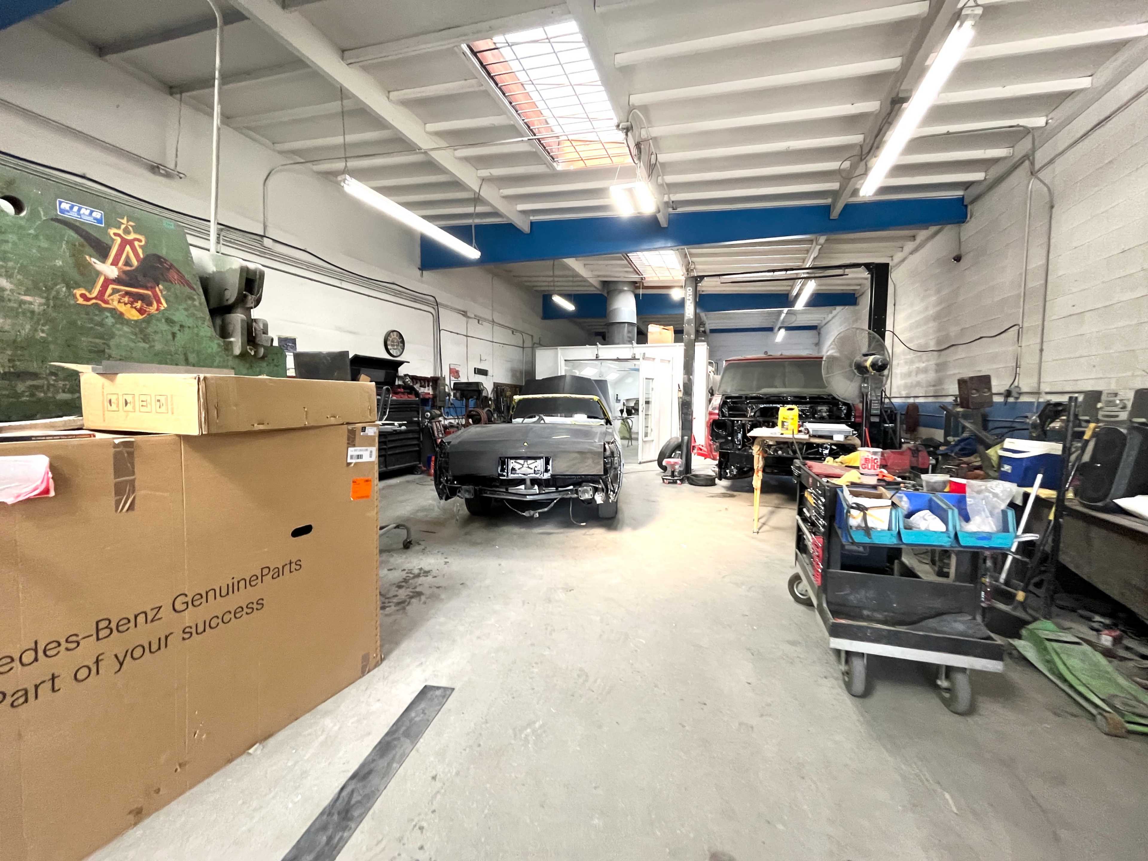 The image shows a garage workshop with several cars in various states of repair, surrounded by tools and equipment organized on counters and carts.