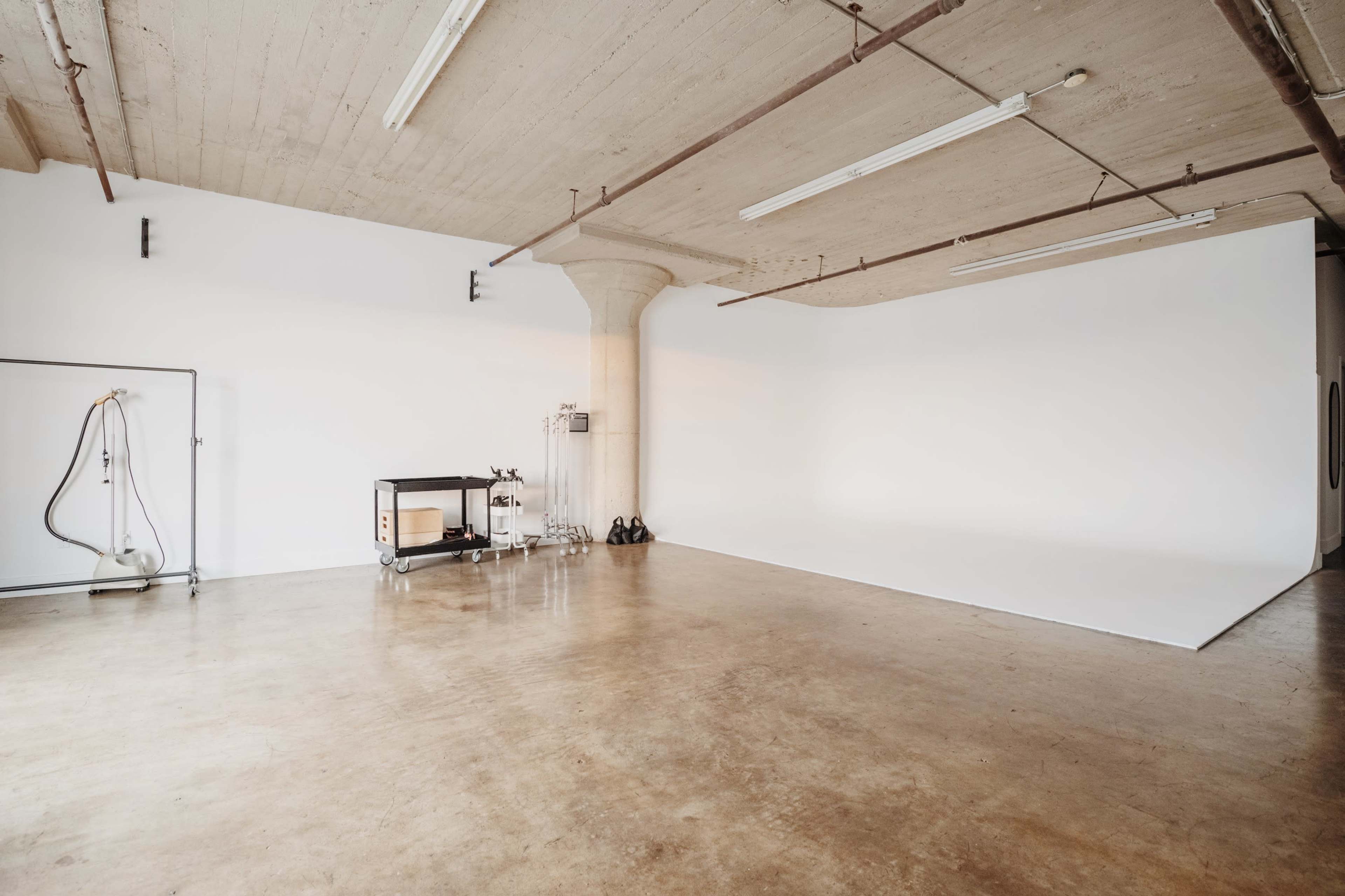 A spacious, minimalistic studio with a plain white backdrop and concrete flooring.