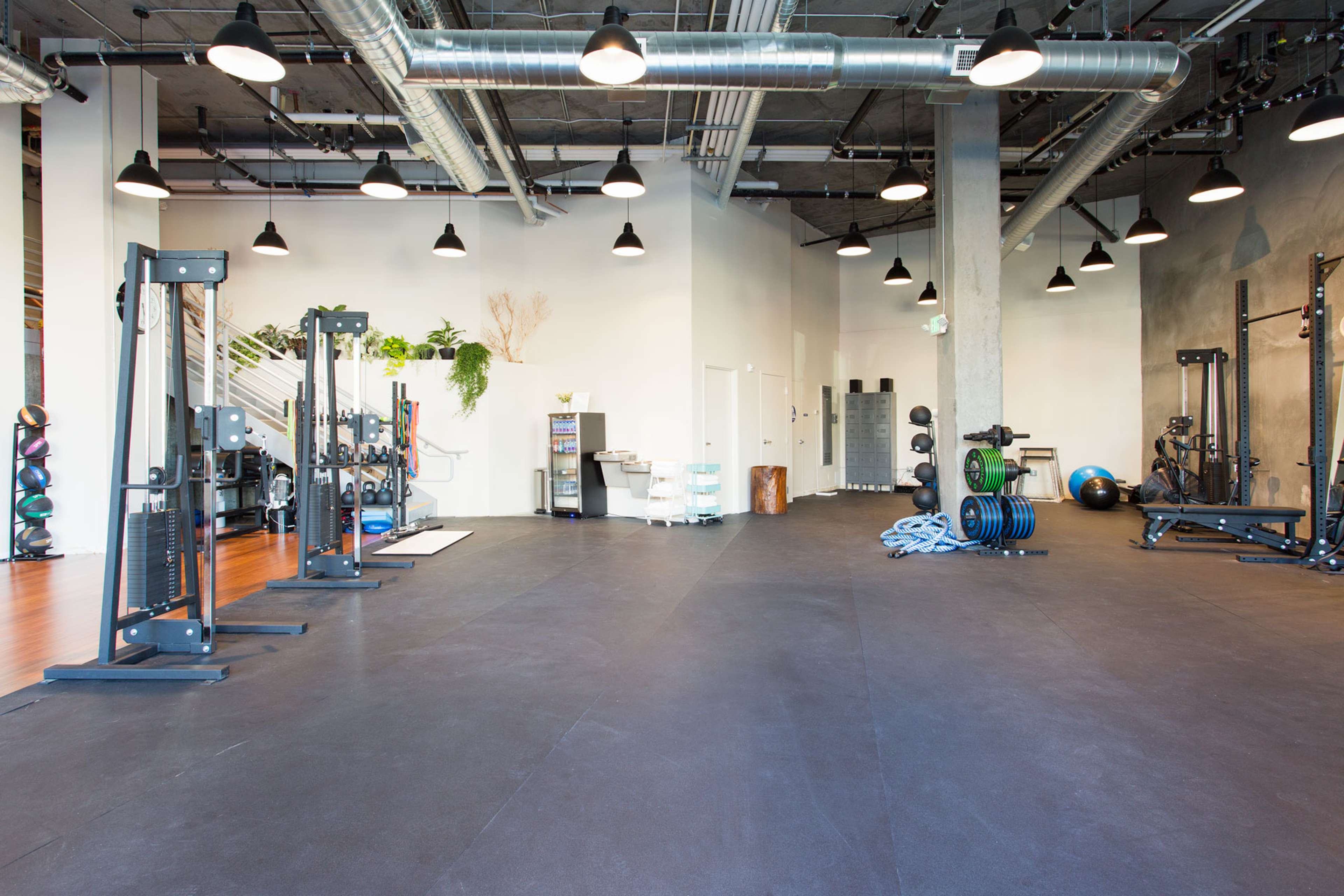 A spacious gym interior with various weightlifting equipment, fitness balls, and exposed ceiling vents.