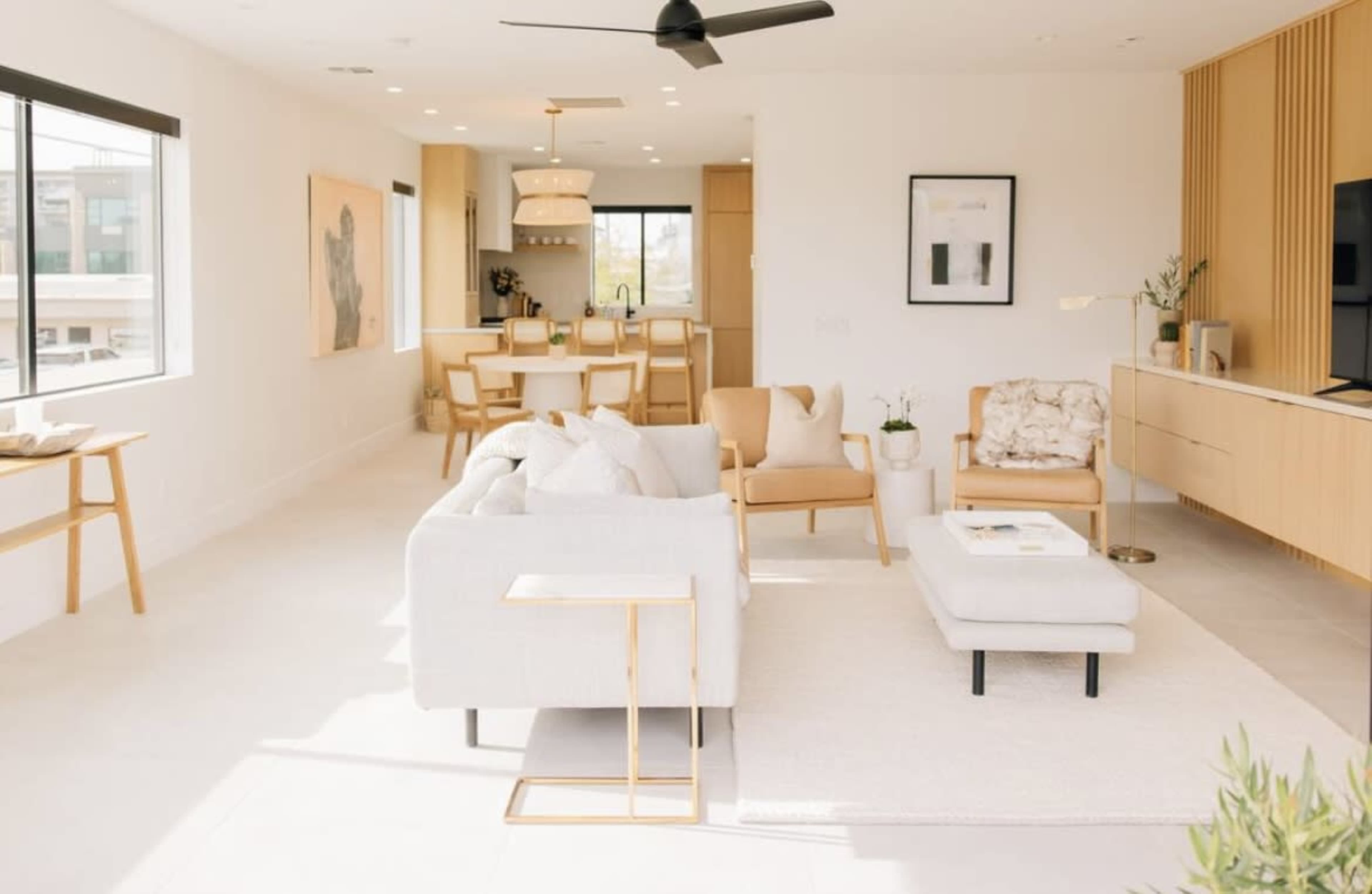 A modern living room with a light color palette, featuring a sectional sofa, armchairs, a coffee table, and a dining area in the background.