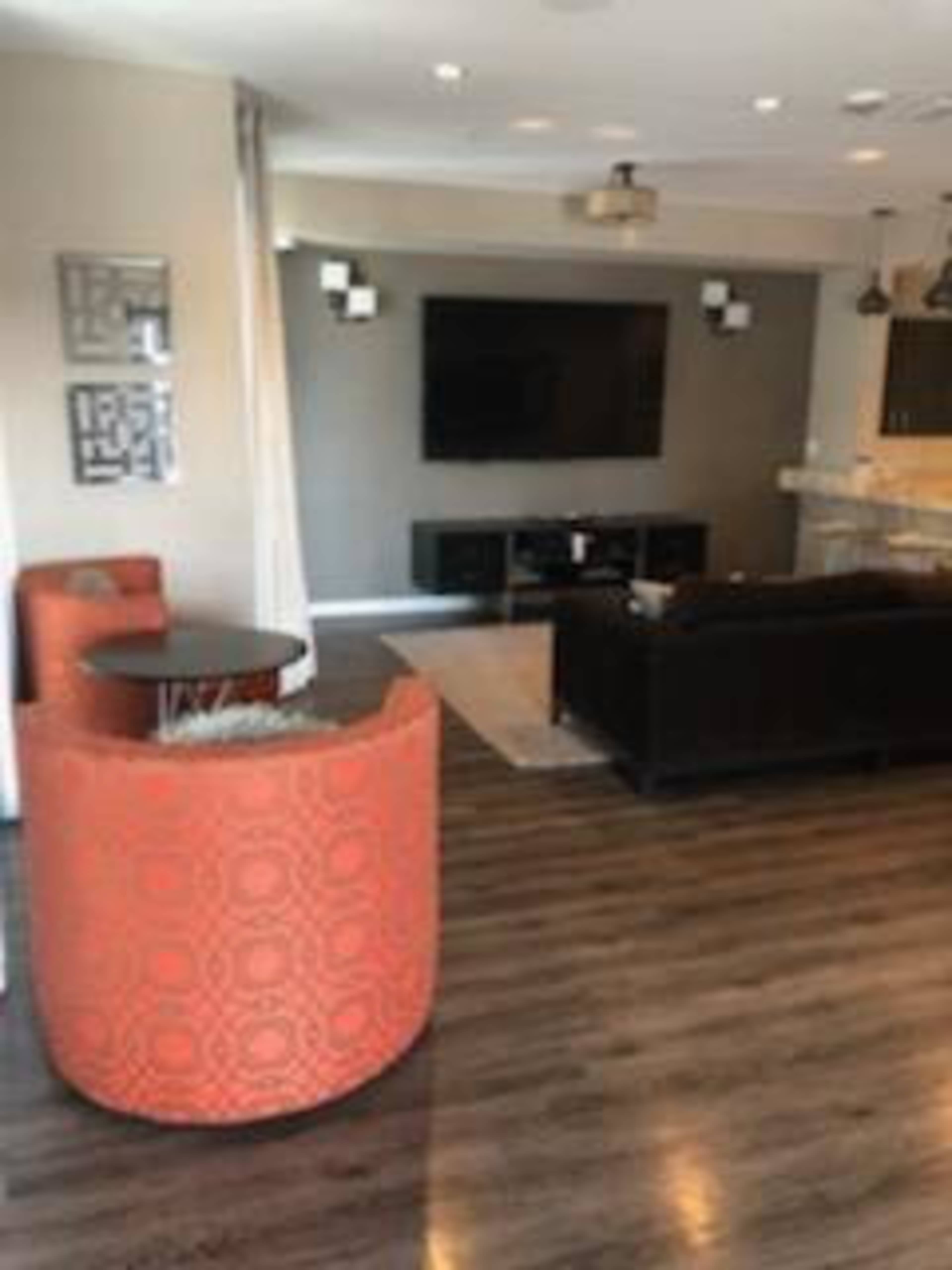 A modern living room with a television mounted on the wall, a dark sofa, an orange armchair, and a dining area with a bar counter.