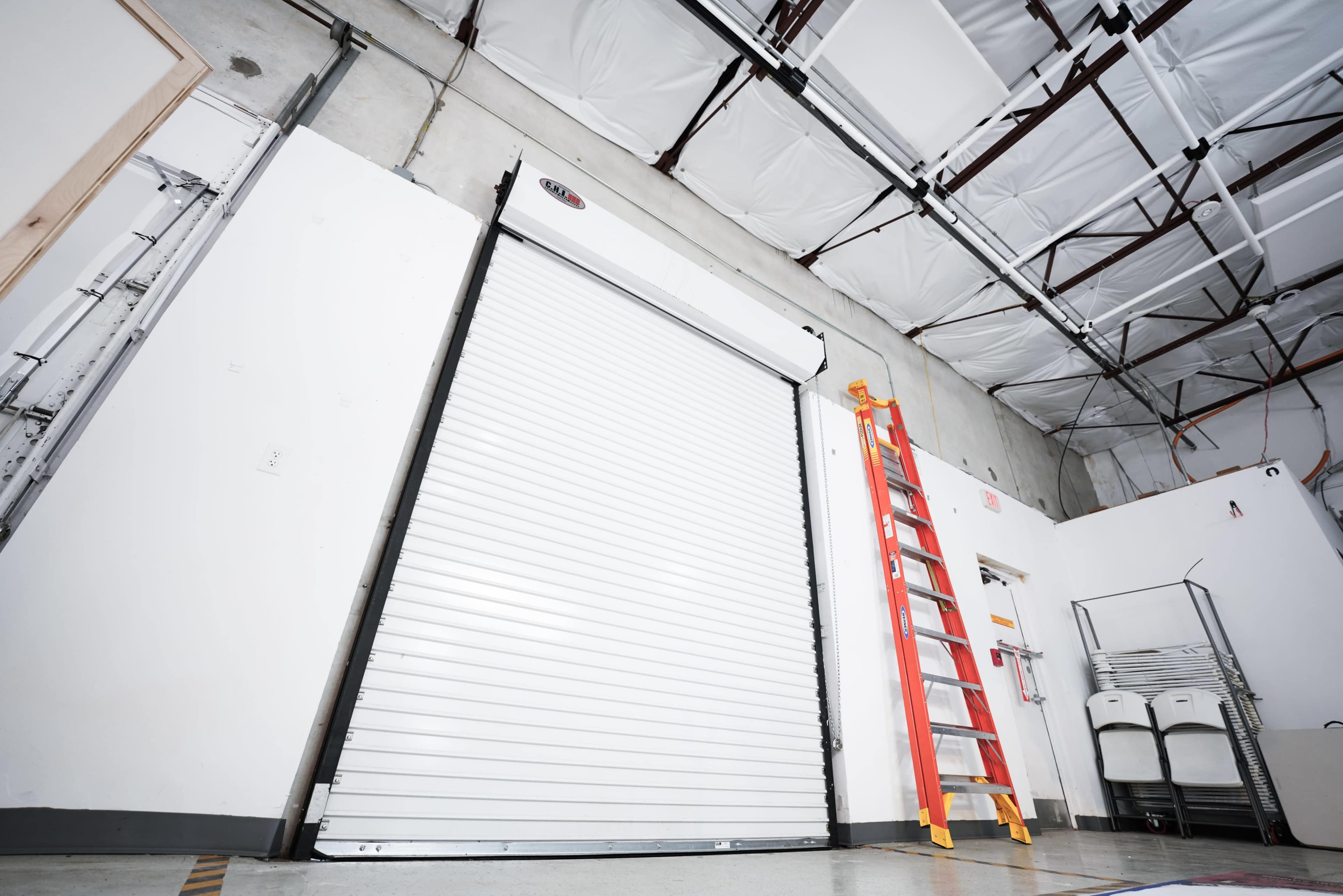 The image shows an industrial space with a roll-up door, a red ladder leaning against the wall, and various items stored nearby.