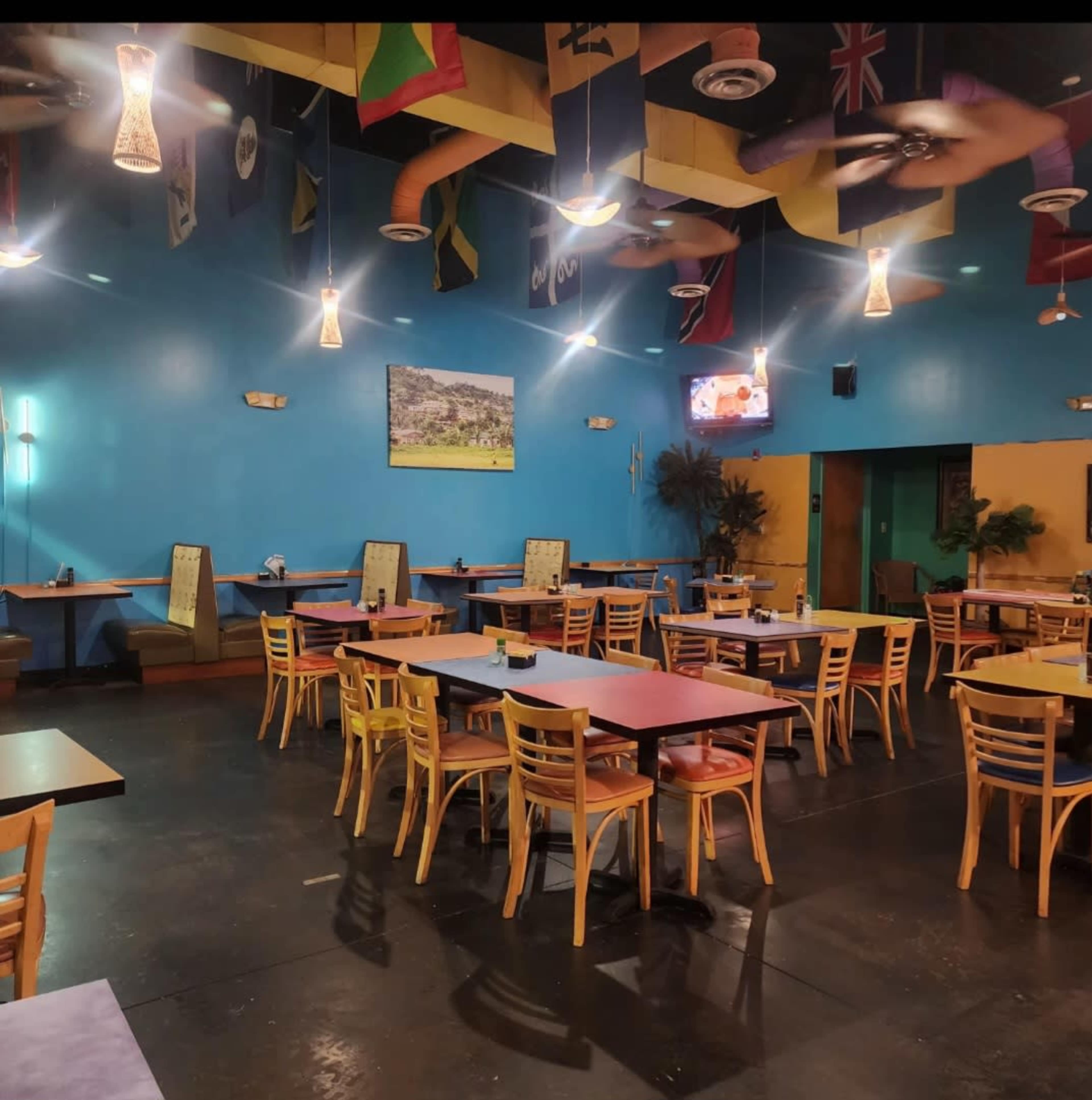 The image shows a restaurant interior featuring colorful walls, tables with wooden chairs, and a ceiling decorated with various international flags.