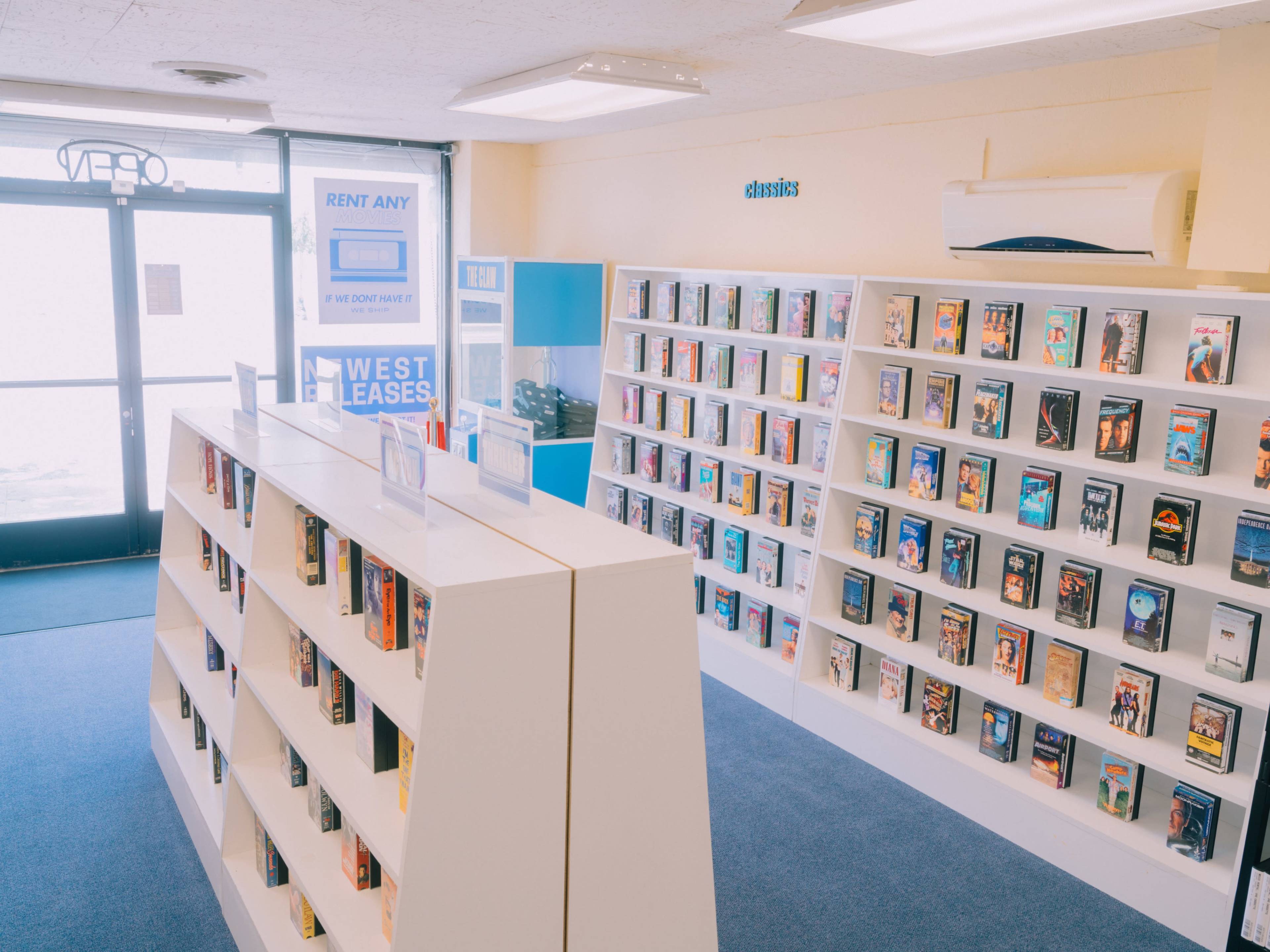 The image shows an open video rental store featuring shelves filled with various VHS tapes arranged neatly along the walls.