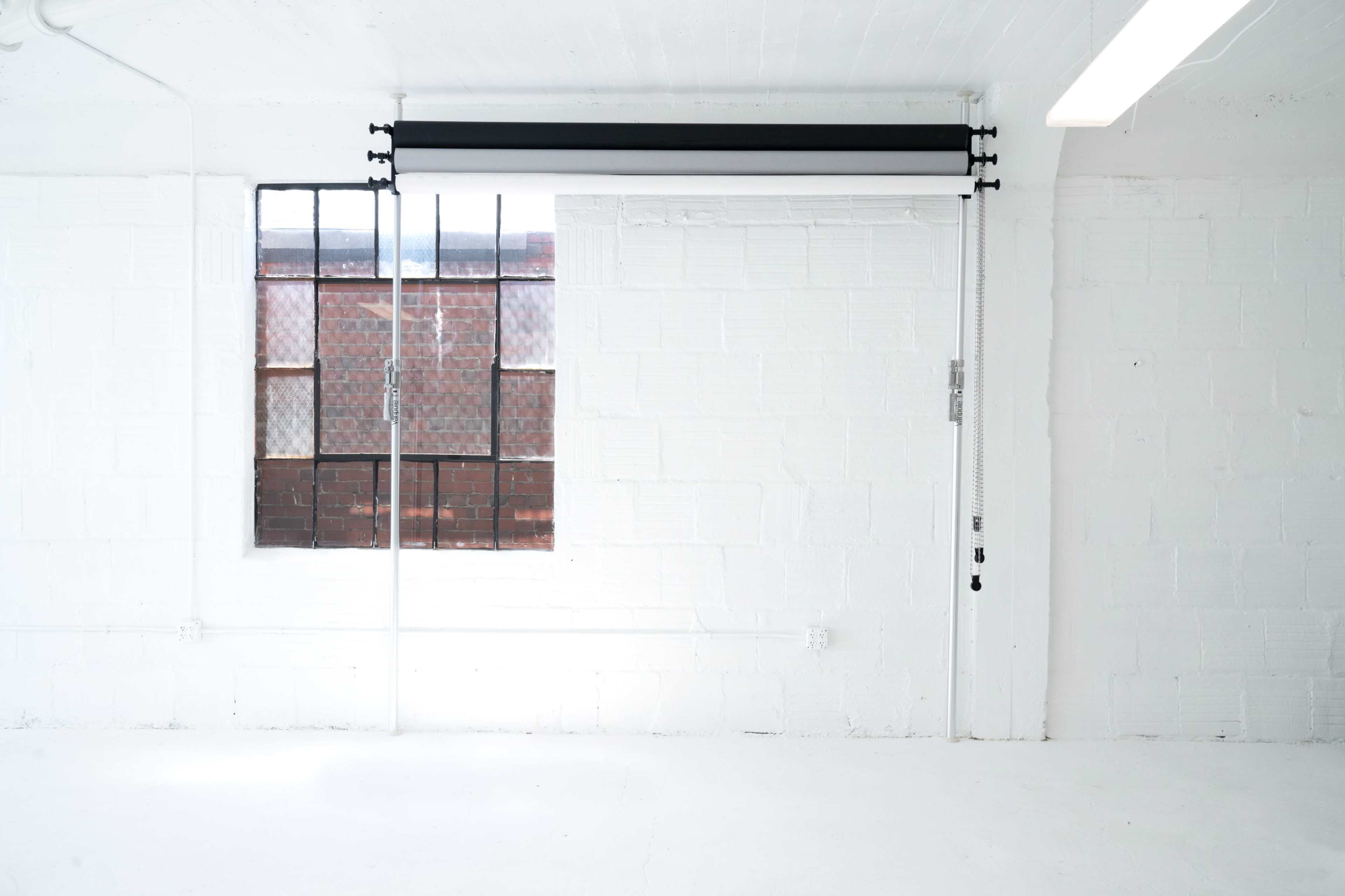 A minimalist white room with a large window featuring black window treatments and a view of a brick building outside.