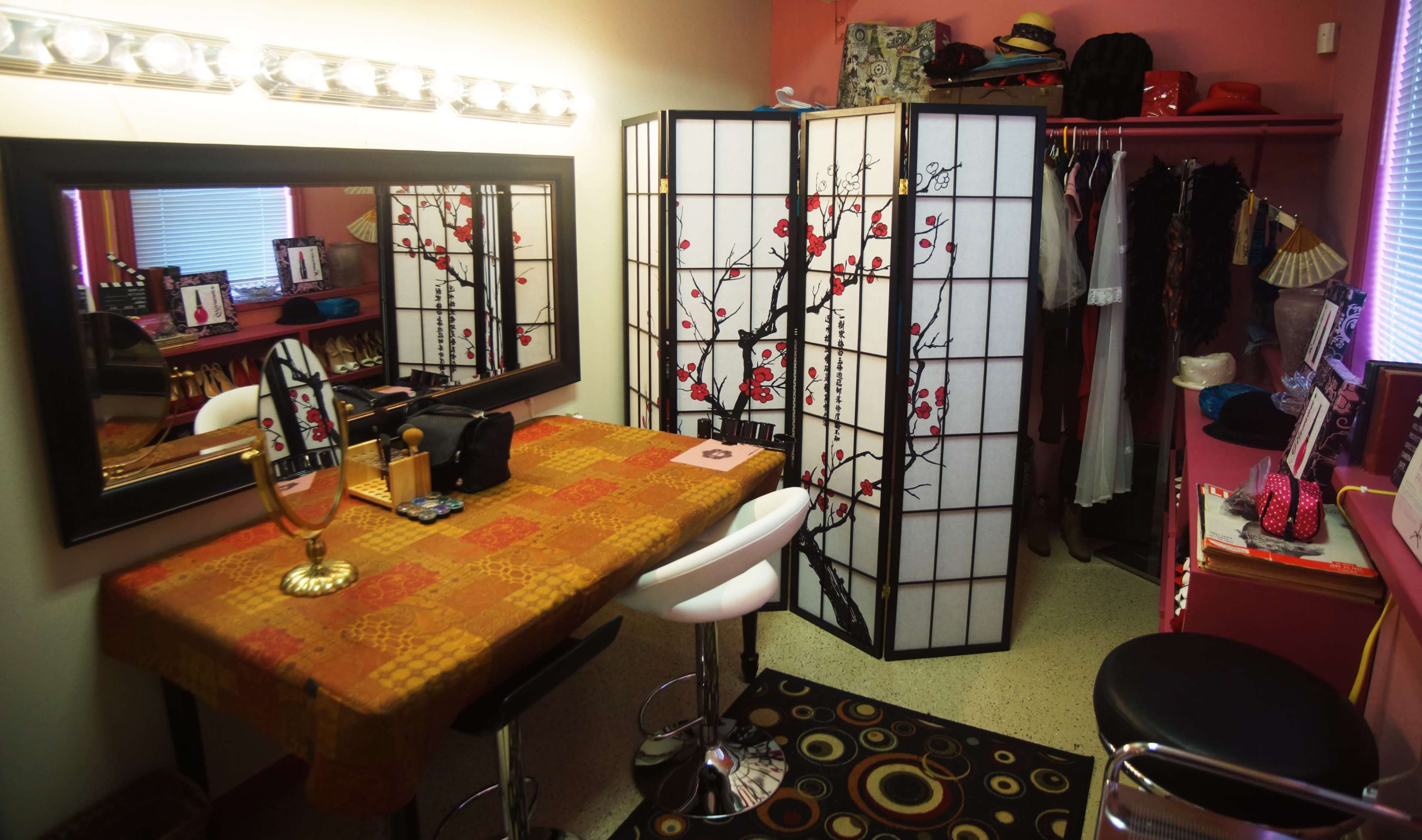 A small dressing area featuring a mirror, a table with a decorative cloth, a folding screen, and clothing hanging on a rack.