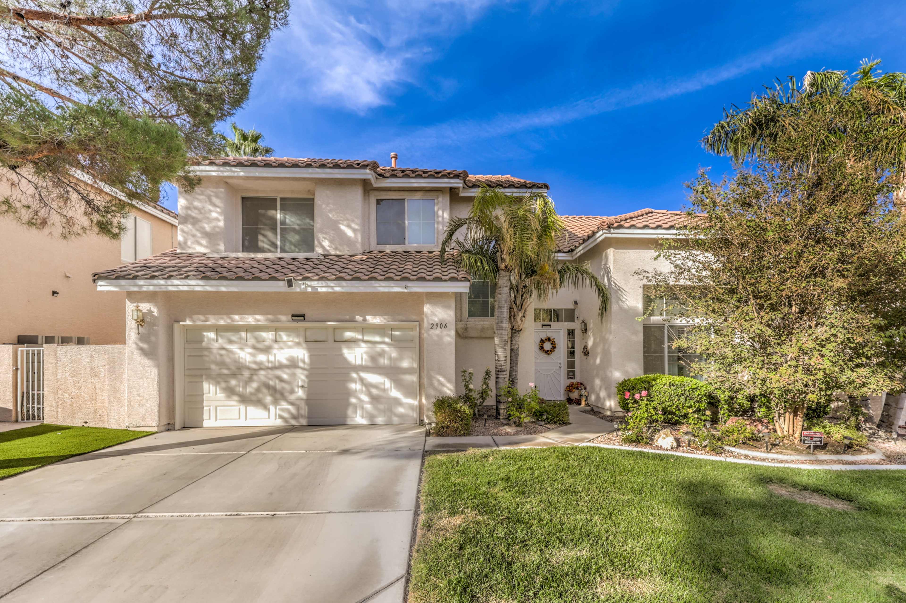 A two-story house with a tile roof, palm trees, and a well-maintained front yard.