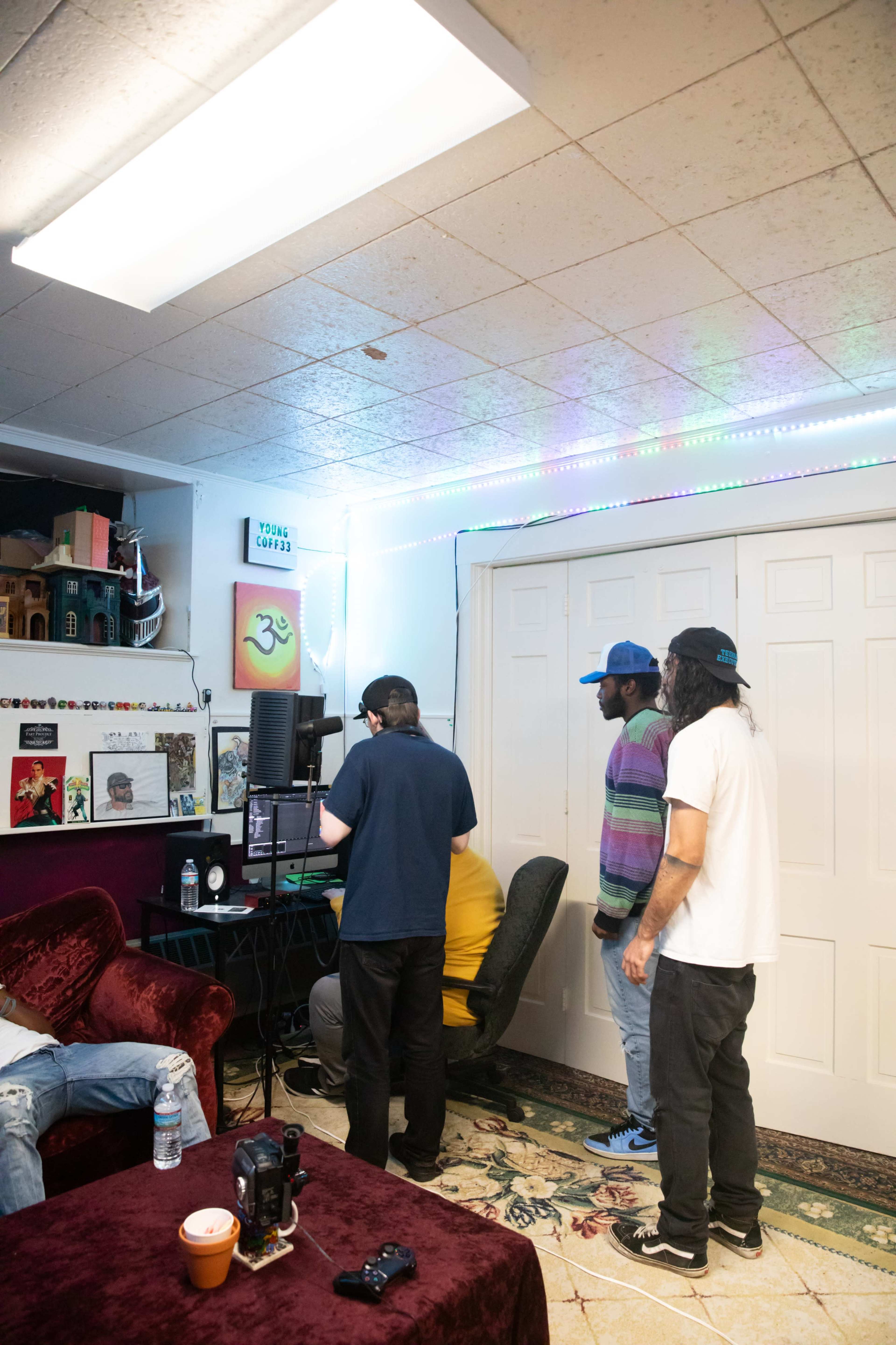 A group of four people stand around a computer in a room decorated with colorful lights and art.