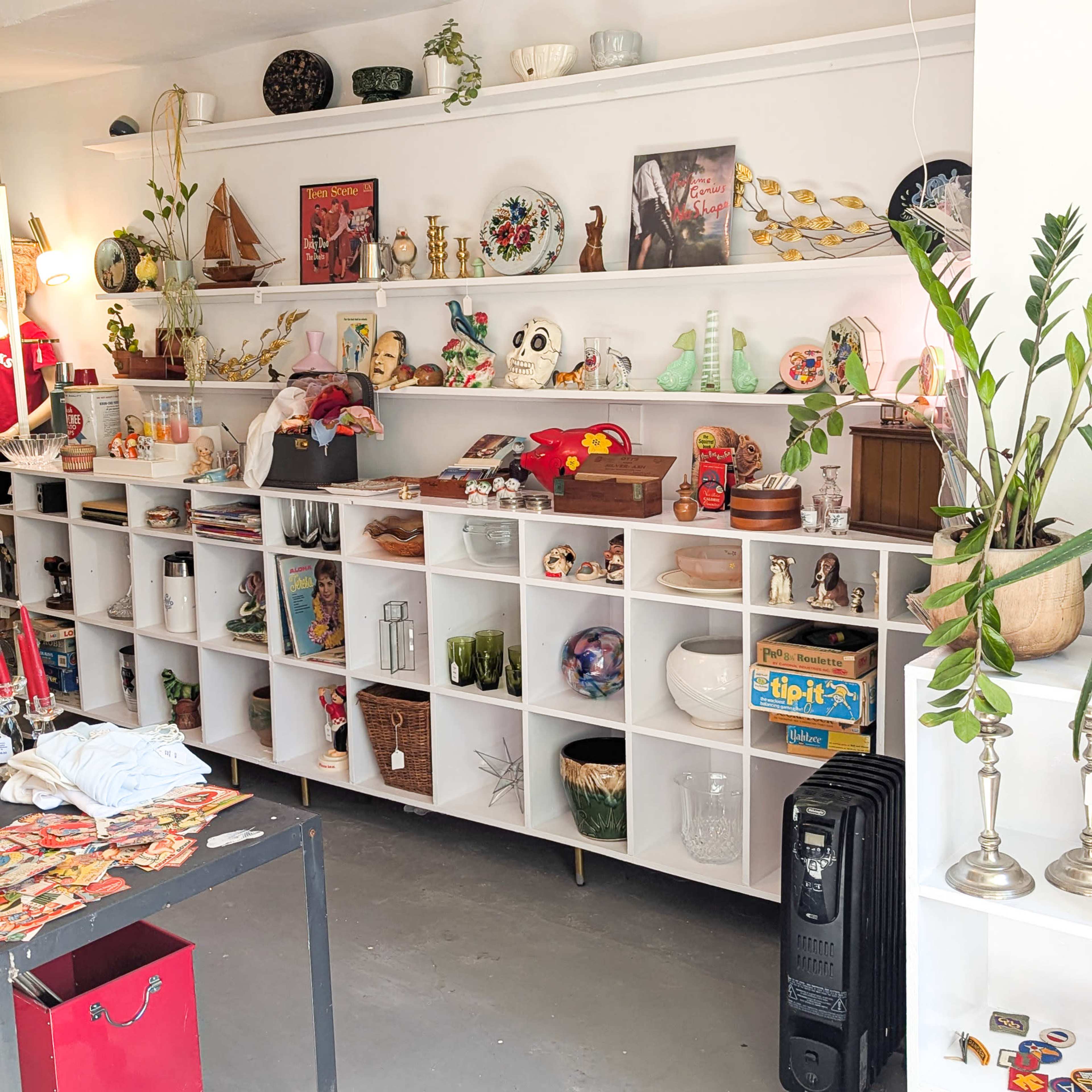 The image shows a display of various vintage items arranged on white shelves, including decorative pieces, glassware, and collectibles.