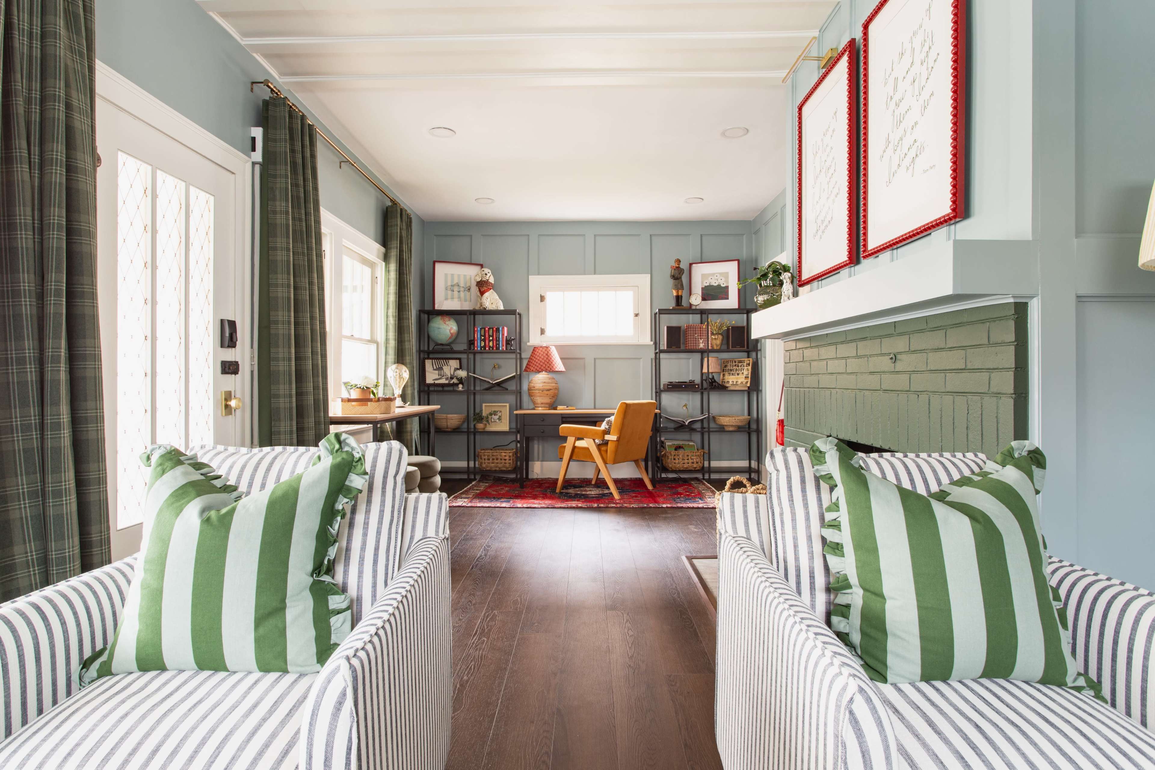 The image shows a stylish living room with two striped armchairs with green pillows, a wooden desk positioned against a light blue wall, and a cozy ambiance created by a mix of decorative elements and natural light.