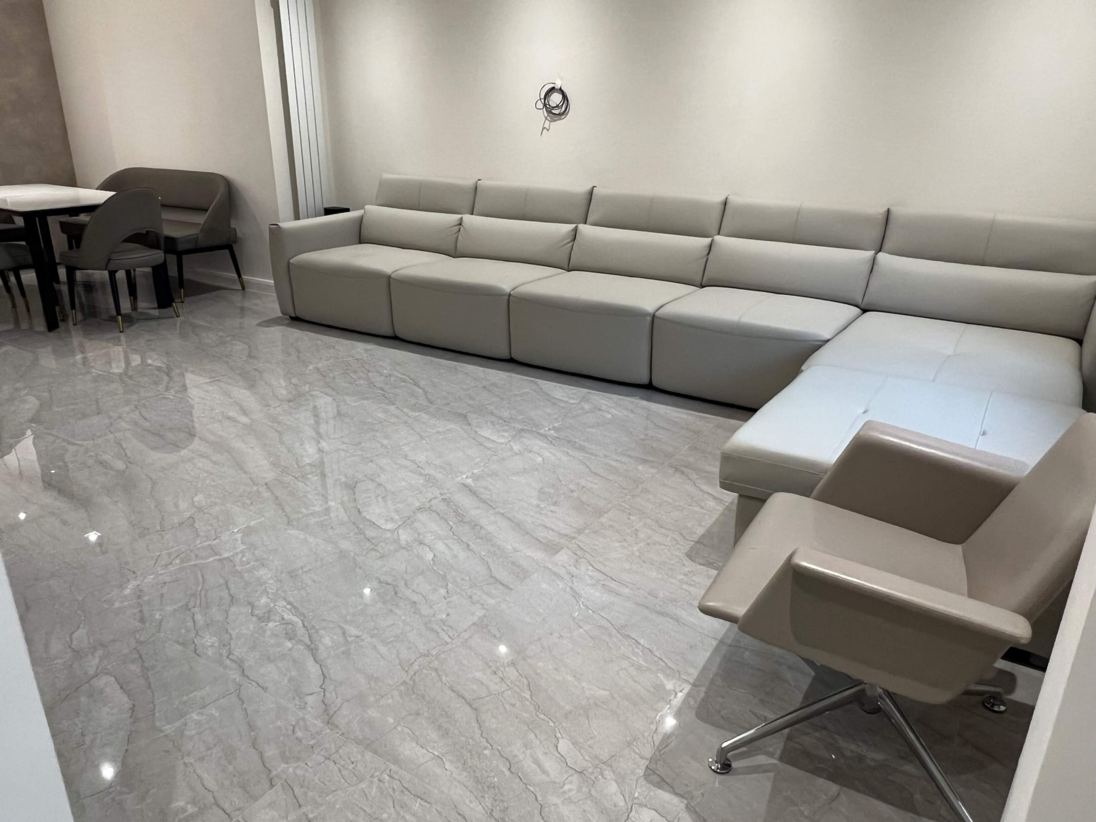 The image shows a modern living room featuring a large grey sectional sofa, a sleek armchair, and a polished marble floor.