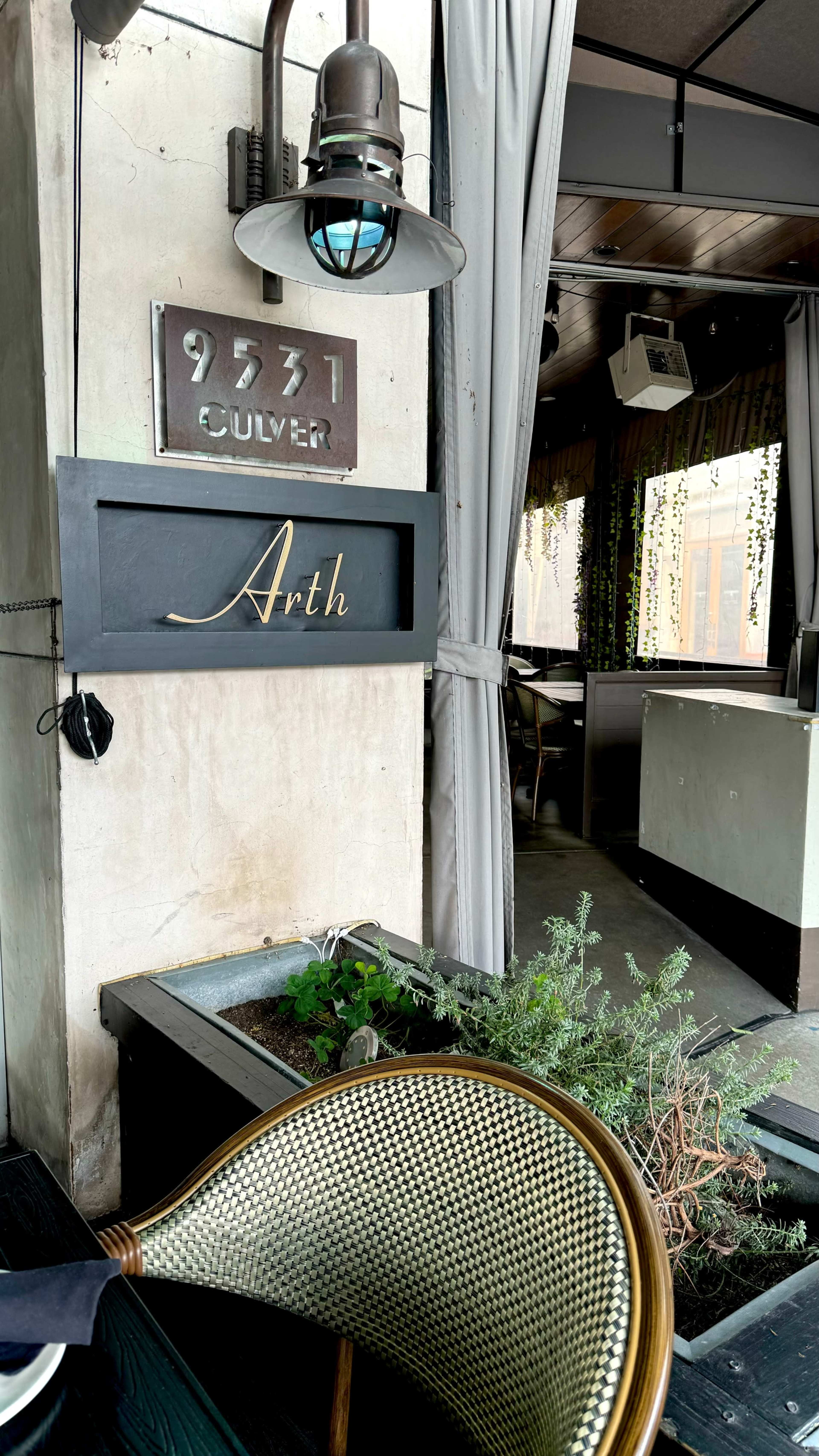 The image shows the exterior of a restaurant named "Arth," with a decorative sign and a planter featuring greenery.