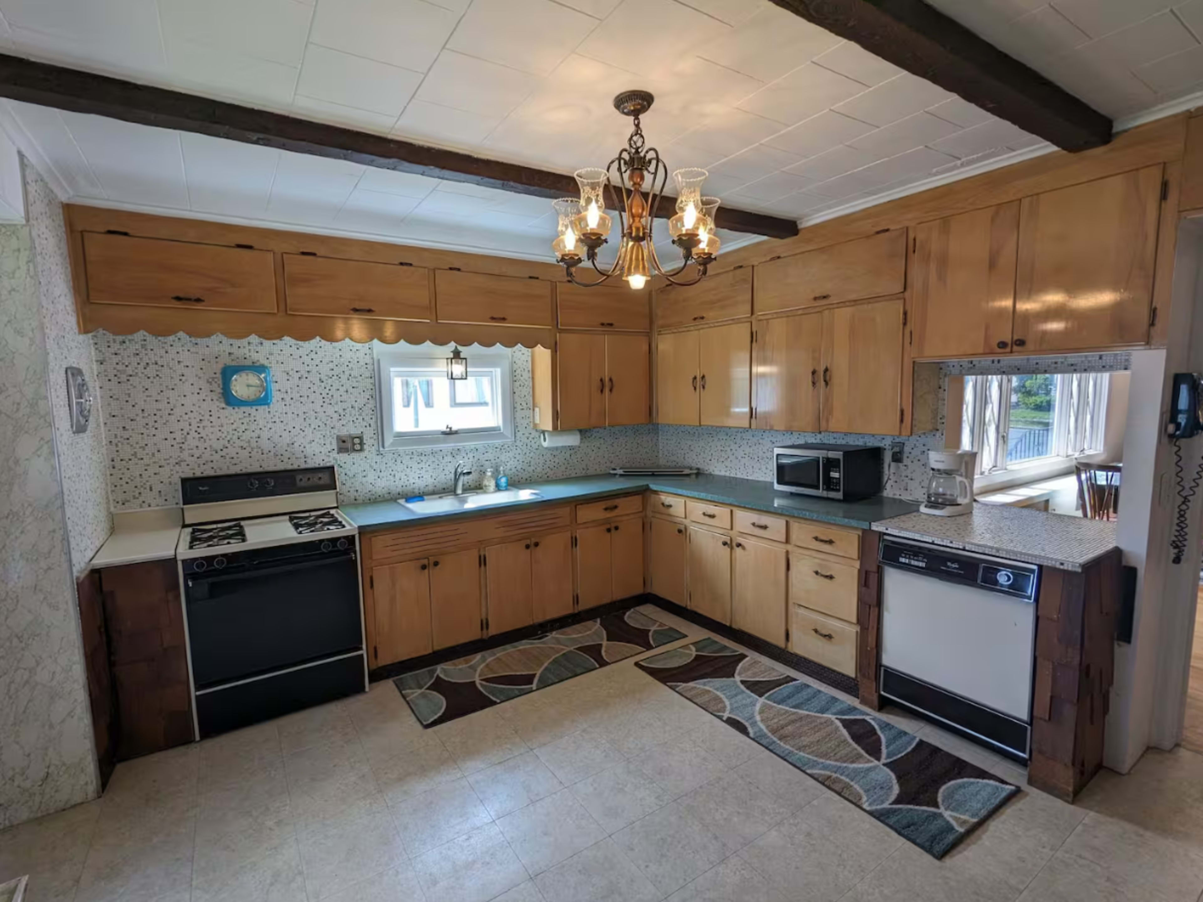 The kitchen features wooden cabinetry, a patterned rug, and a chandelier, with appliances including a stove, microwave, and dishwasher.