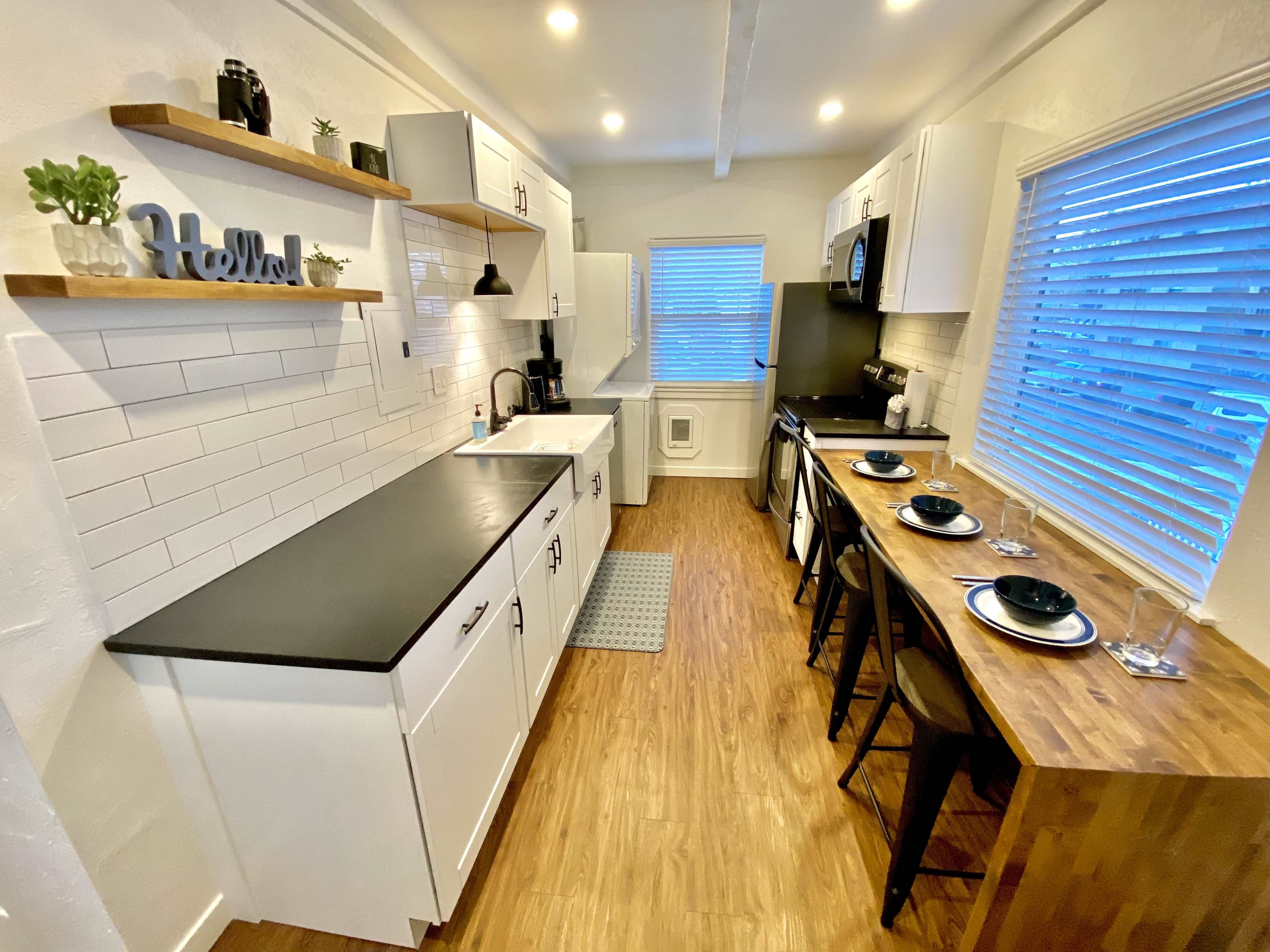 A modern kitchen with white cabinets, a black countertop, and a dining area with wooden seating.