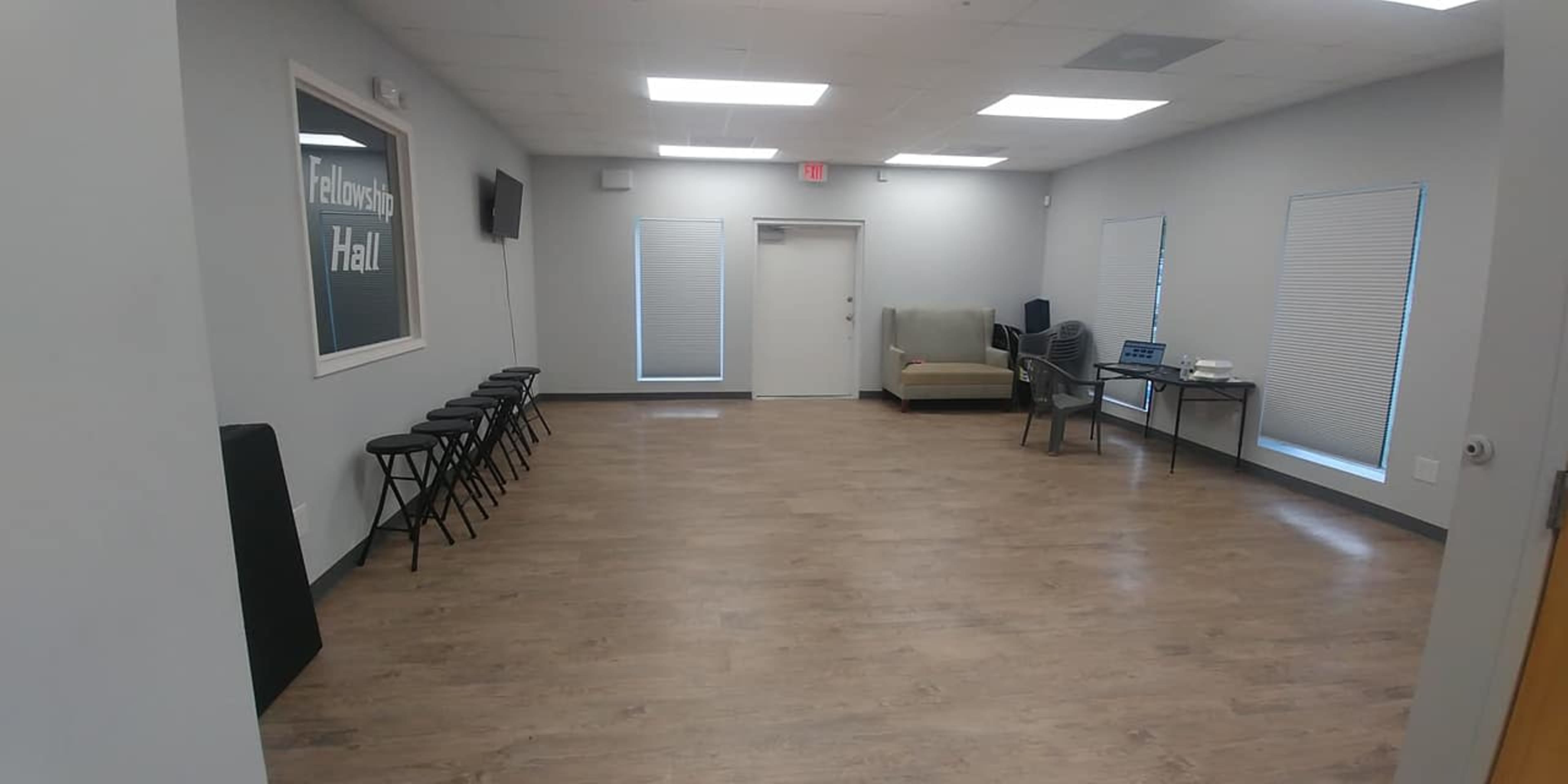 A large, empty room with a few chairs and a couch along the walls, and a table set up with a laptop and other items.