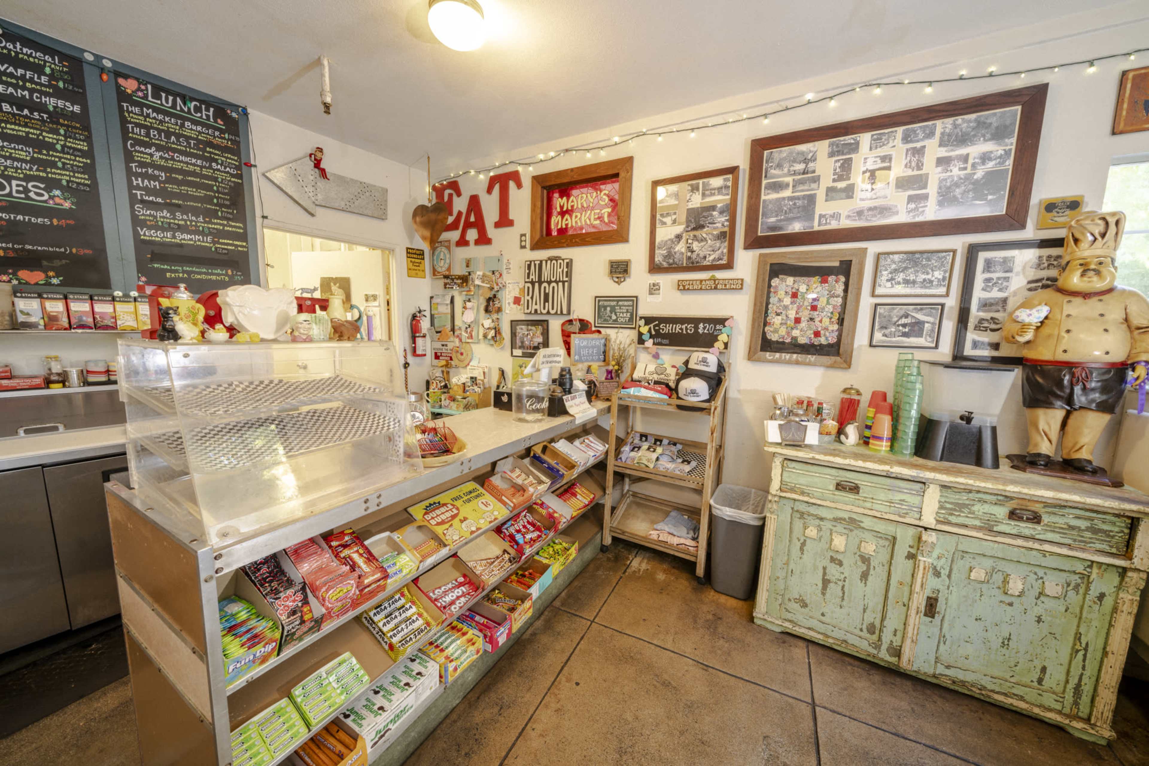 The image shows a quaint counter area of a café featuring a display case with snacks, a menu board, and a wall adorned with vintage photographs and memorabilia.