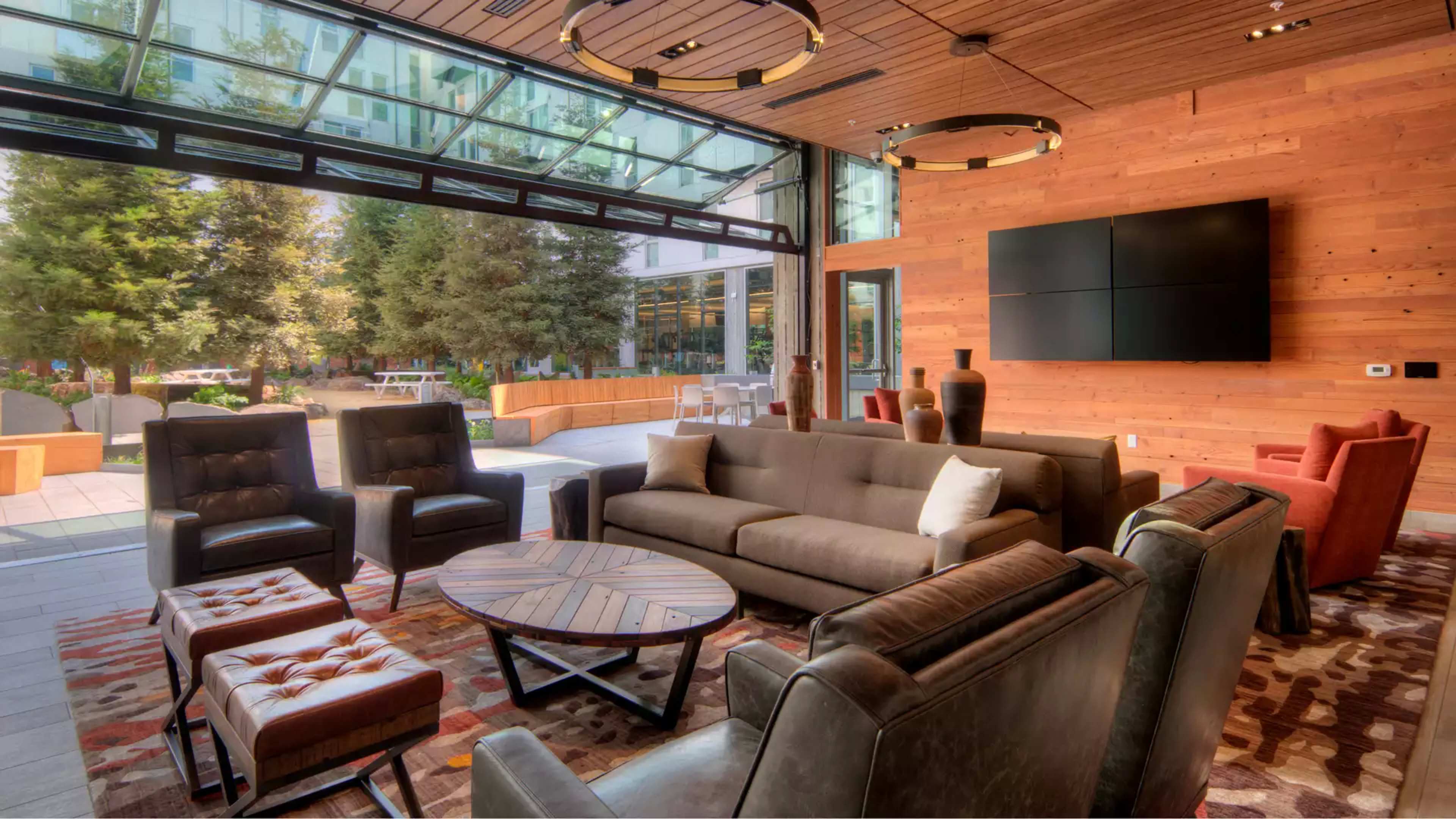 A modern lounge area with a mix of seating options, large windows opening to an outdoor space, and wooden accents on the walls.