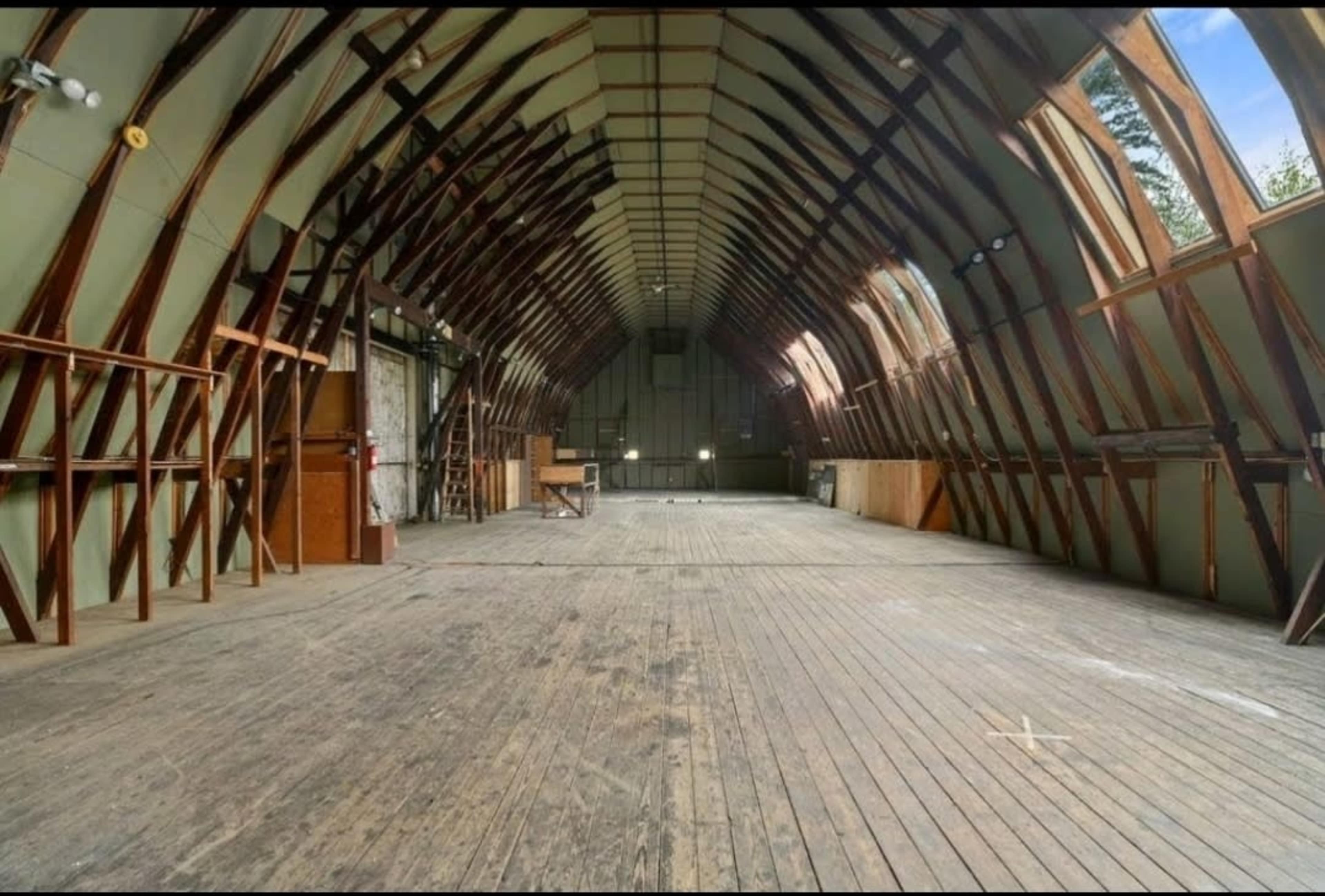 A spacious, unfinished interior of a building with high arched wooden beams and a wooden floor.