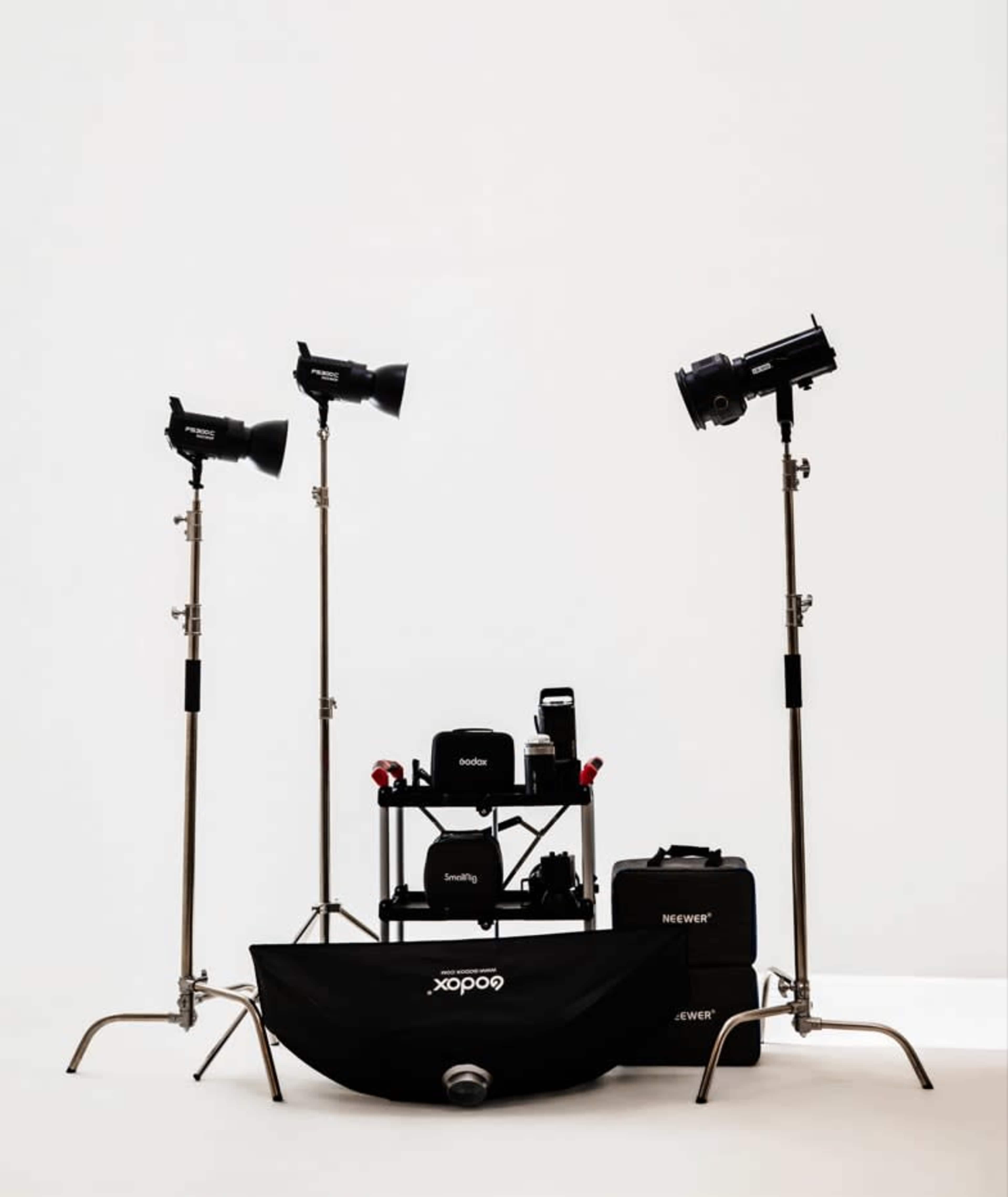 The image shows three studio lights on stands positioned around a central equipment table with various photography gear.