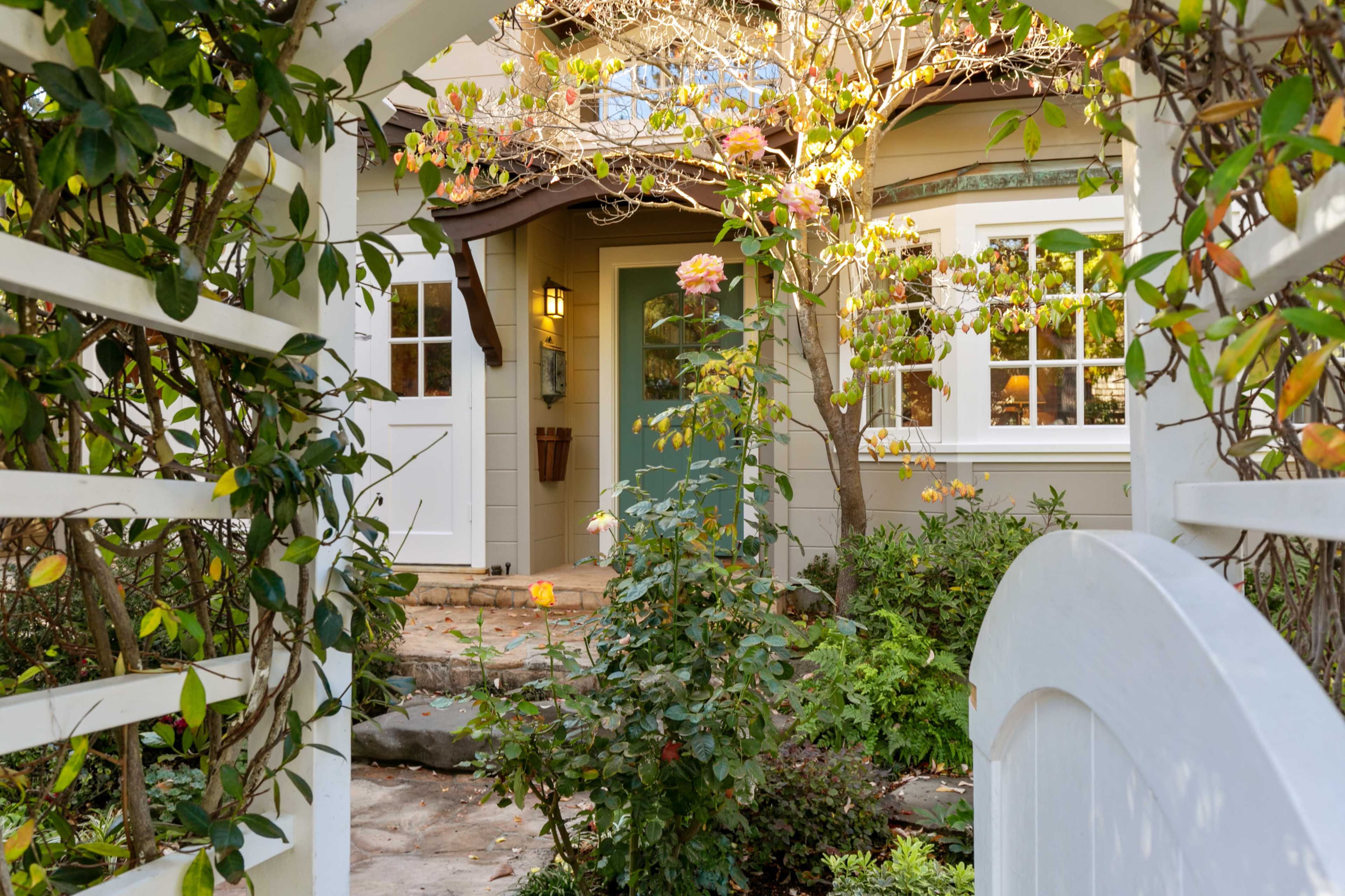 A pathway leads to a quaint home with a green door, surrounded by flowering plants and greenery.