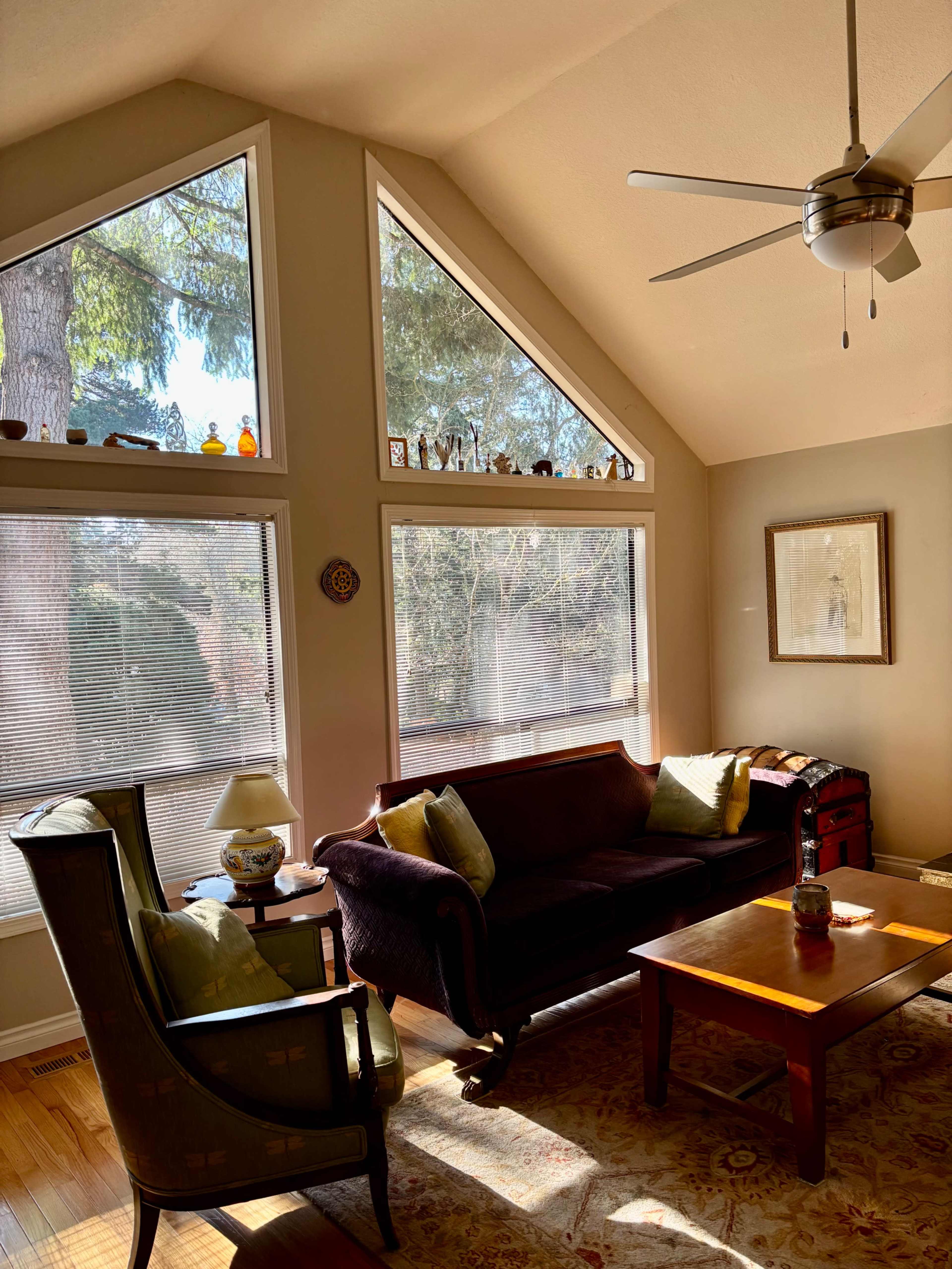 A living room features a dark sofa and an armchair, with large triangular windows allowing natural light to illuminate the space.