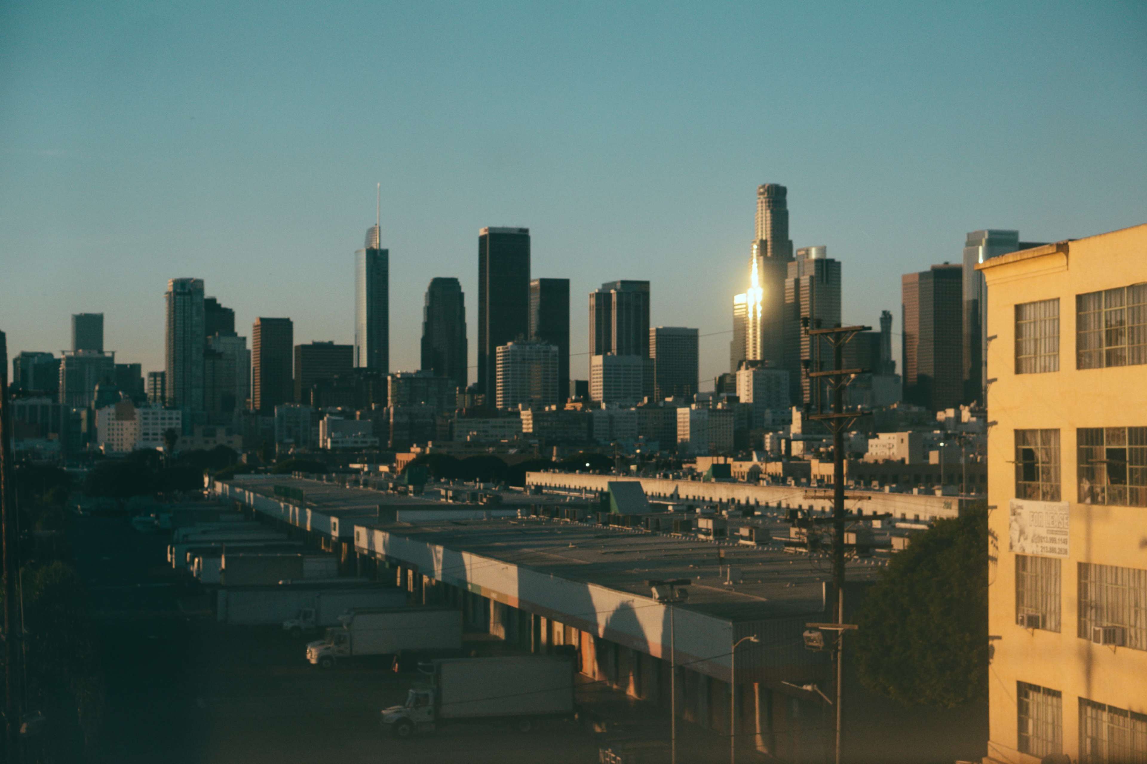 The image shows a skyline of tall buildings in a city during sunset, with a shining reflection on one of the skyscrapers.