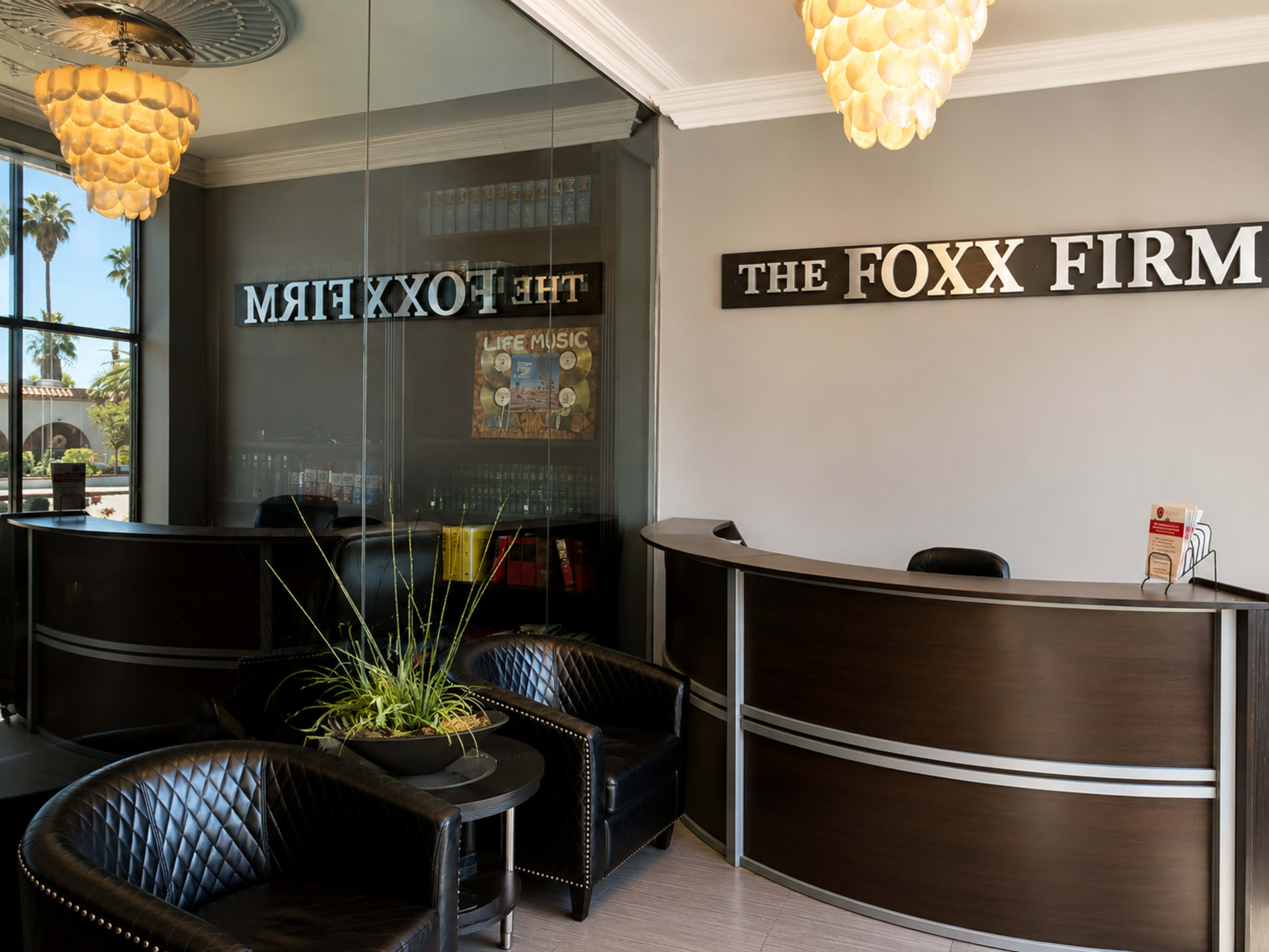 The image shows a modern reception area with a curved desk, dark chairs, and large windows providing natural light.