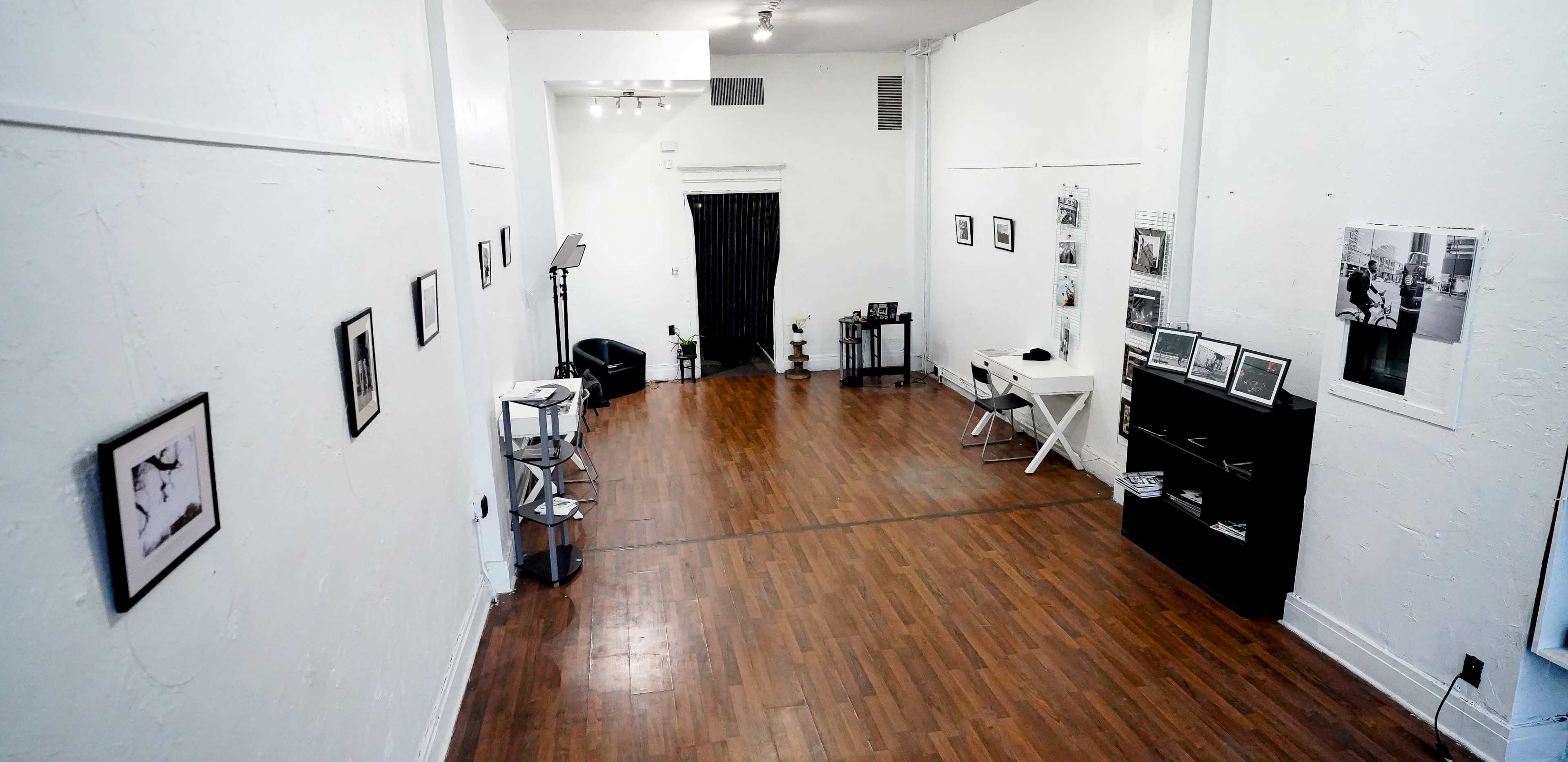 A spacious gallery with white walls, wooden flooring, and framed photographs displayed along the sides.
