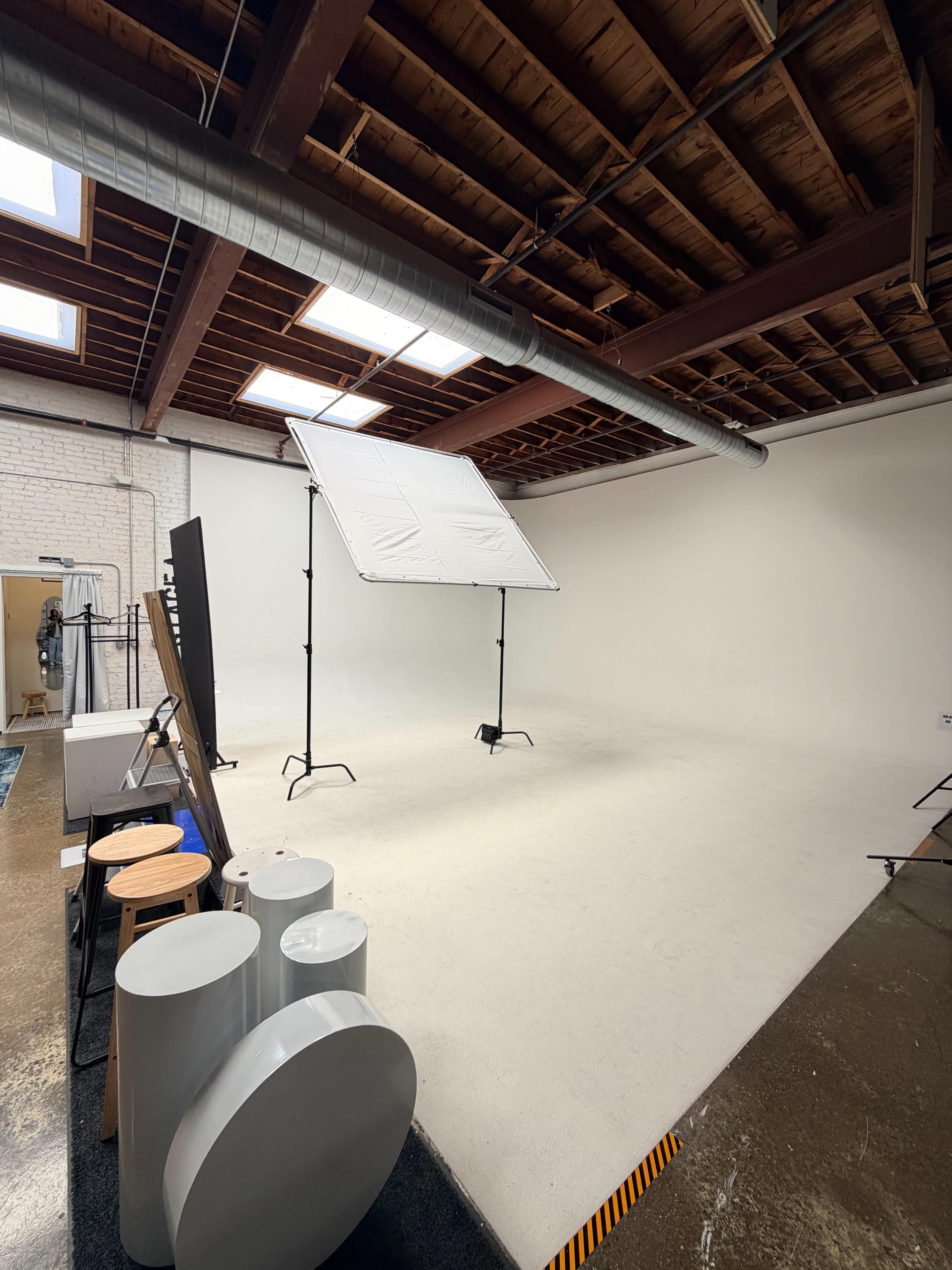 The image shows a spacious photography studio with a large softbox positioned on a stand, surrounded by various props and equipment against a plain white backdrop.