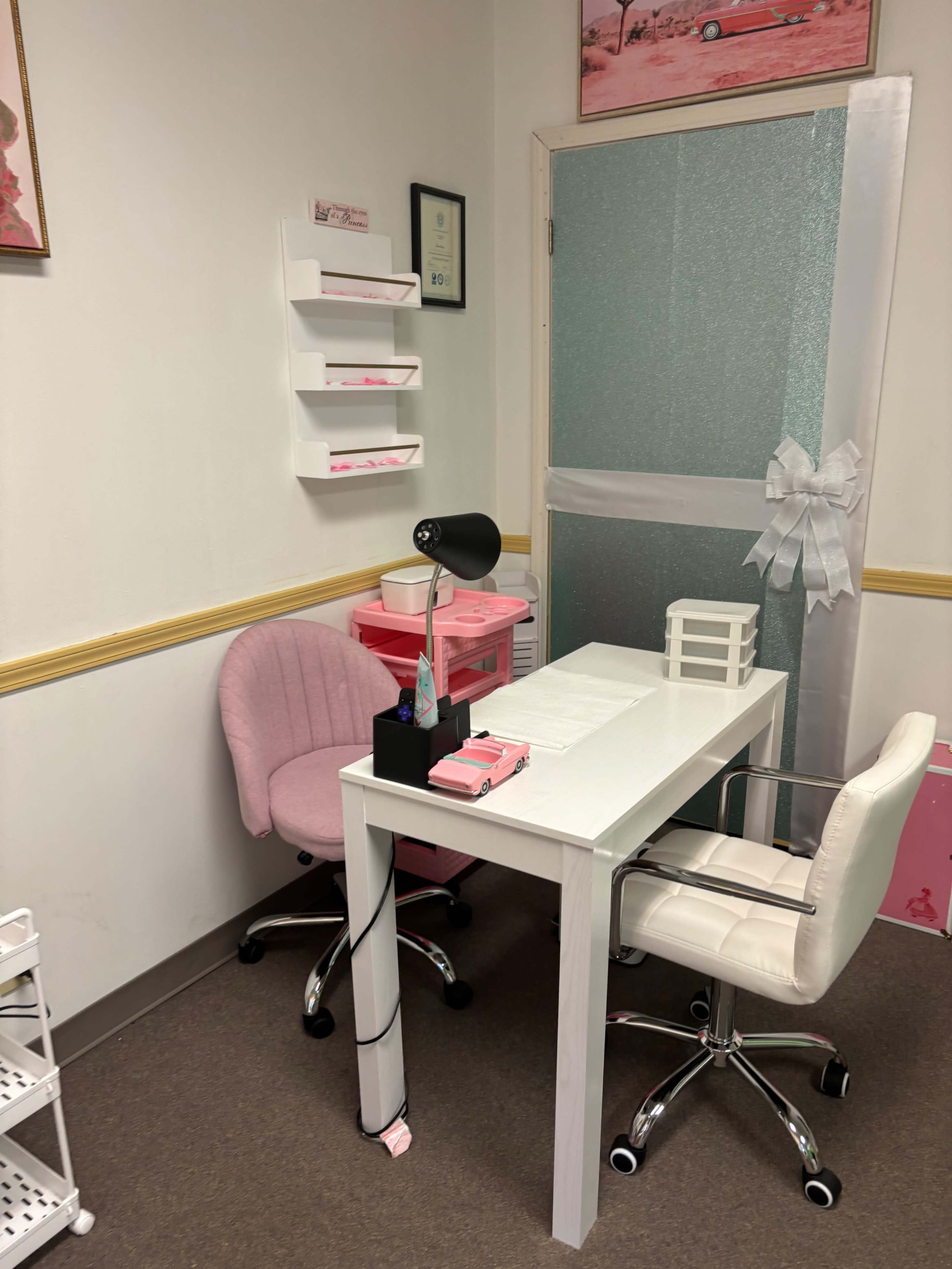 A small office space with a white table, two chairs, and pink decor elements, including a lamp and office supplies.