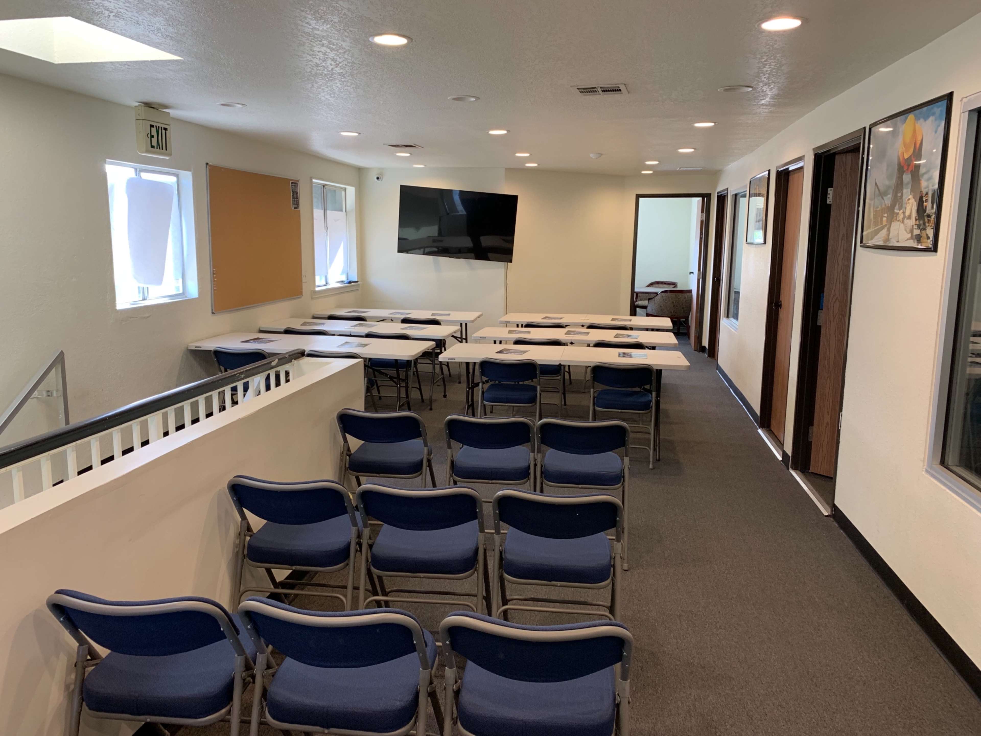 A meeting room arranged with rows of blue chairs facing a wall-mounted television, with tables set up for a presentation.
