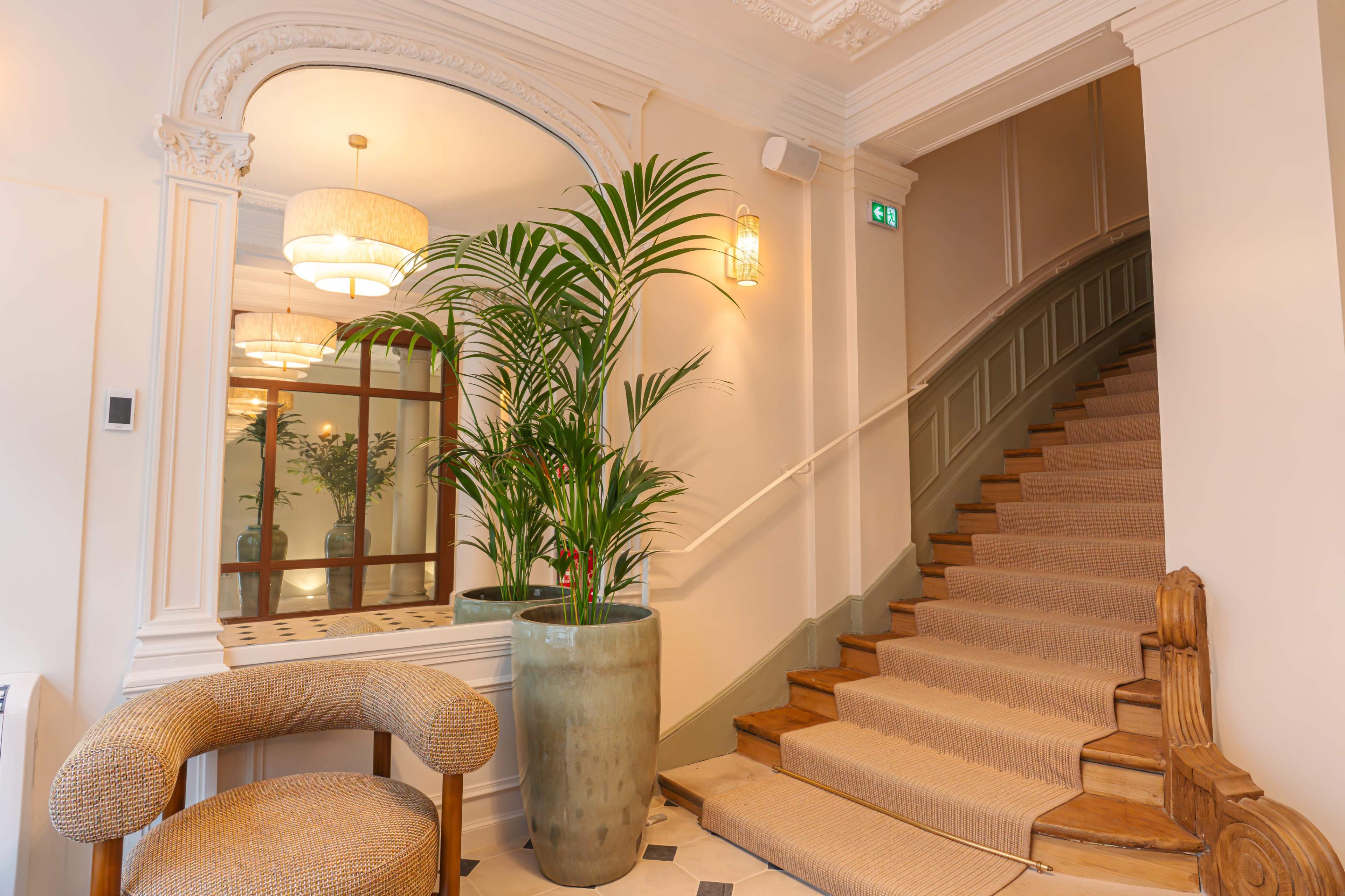 A decorative staircase with a wooden banister is flanked by a large potted plant and a stylish chair in a well-lit entryway.