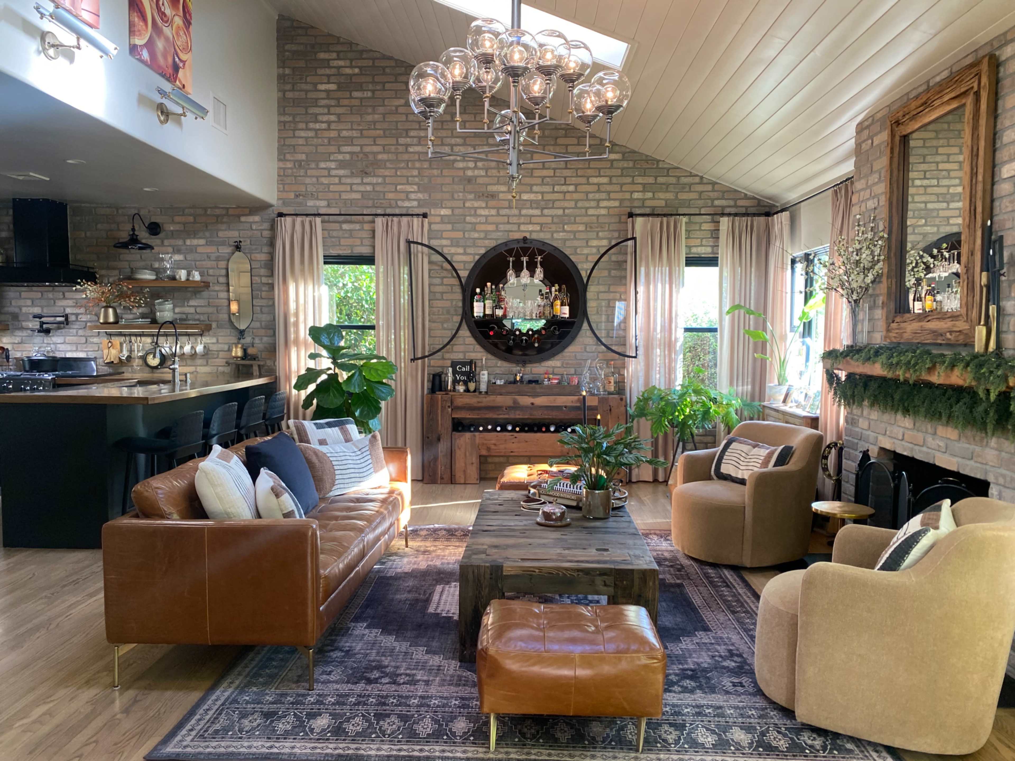 A cozy living room features a brick wall, a wooden coffee table, a bar area, and comfortable seating arrangements with plants and natural light.
