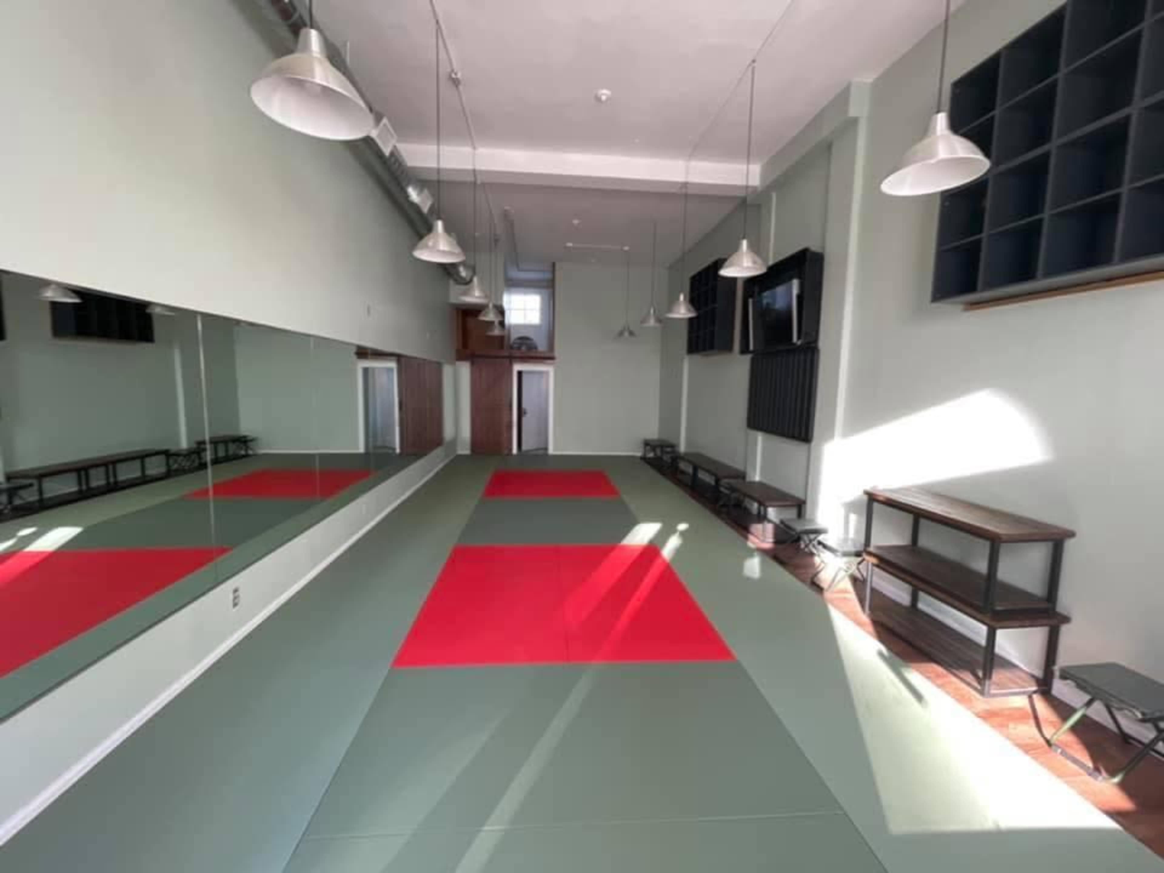 The image shows a martial arts studio with red and green mats, bright overhead lights, and mirrors along one wall.