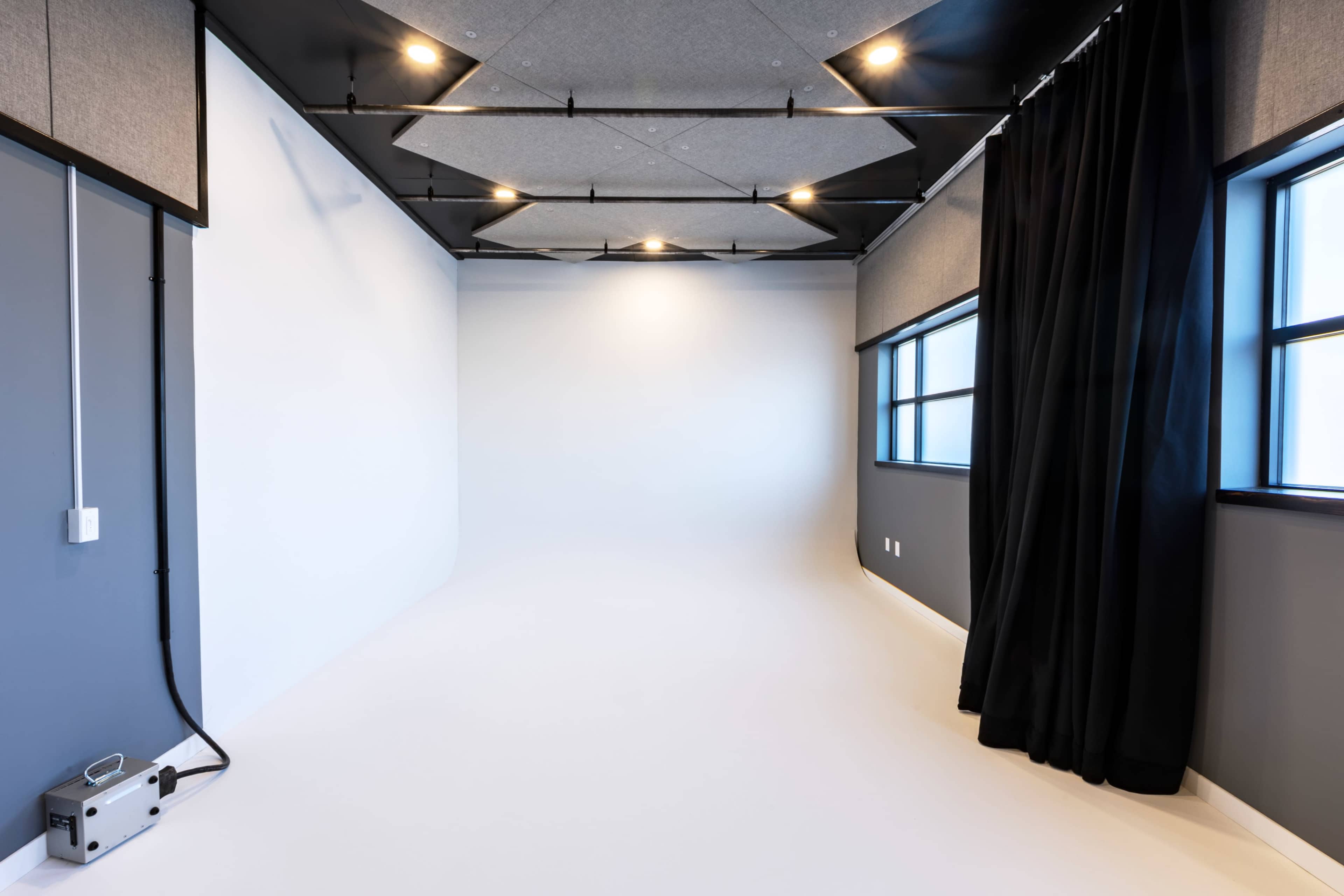 A minimalist studio space with white walls, large windows, and a black curtain in one corner.
