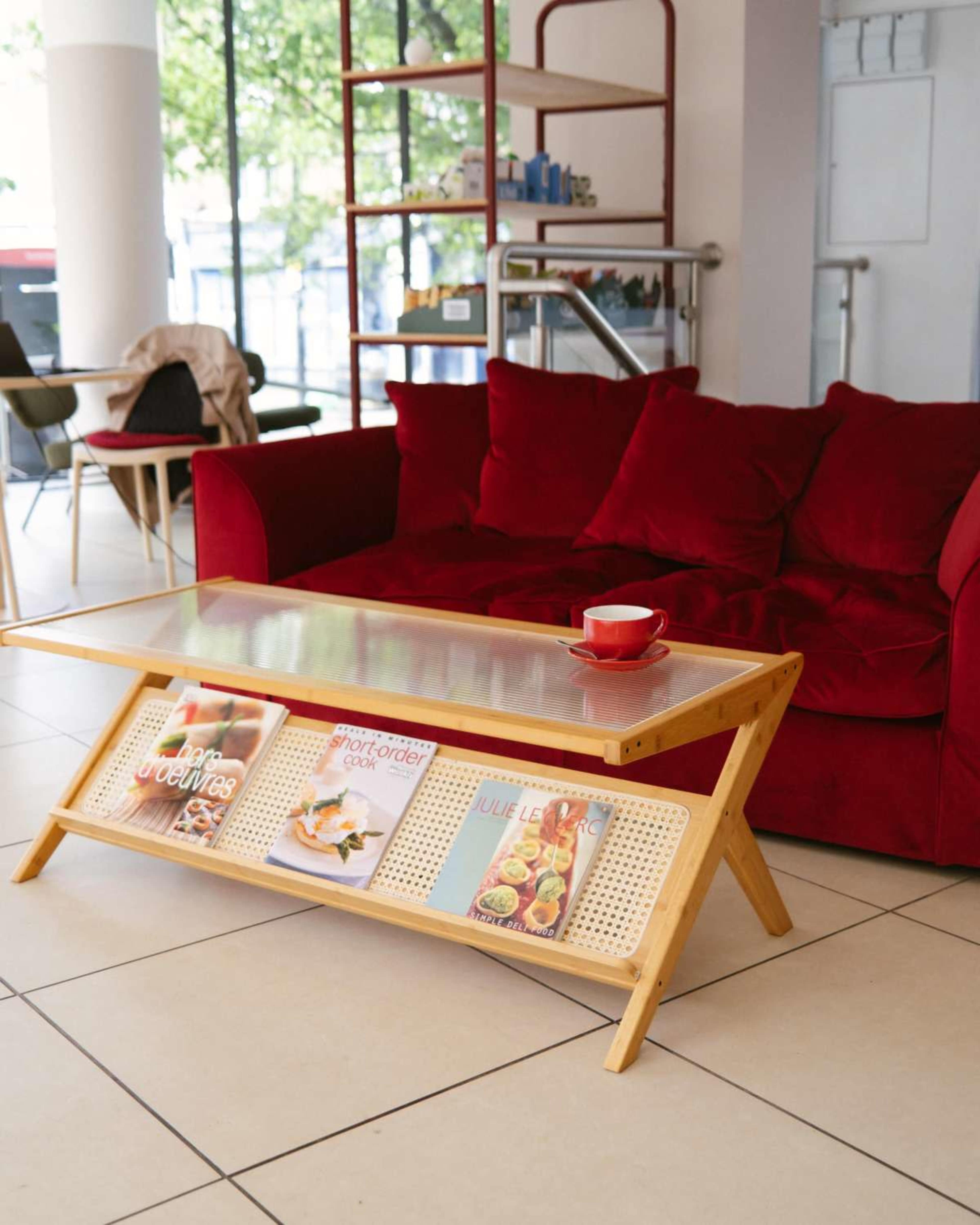 A red couch is paired with a wooden coffee table displaying magazines, set in a bright, modern indoor space.